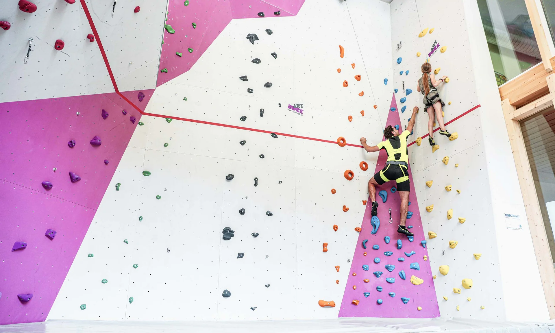 Erwachsener und Kind klettern an farbiger Indoor-Kletterwand