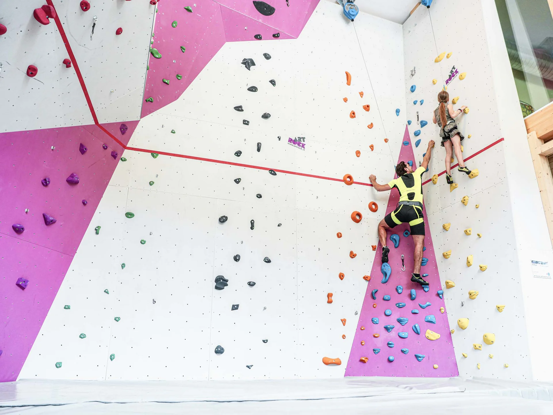 Erwachsener und Kind klettern an farbiger Indoor-Kletterwand