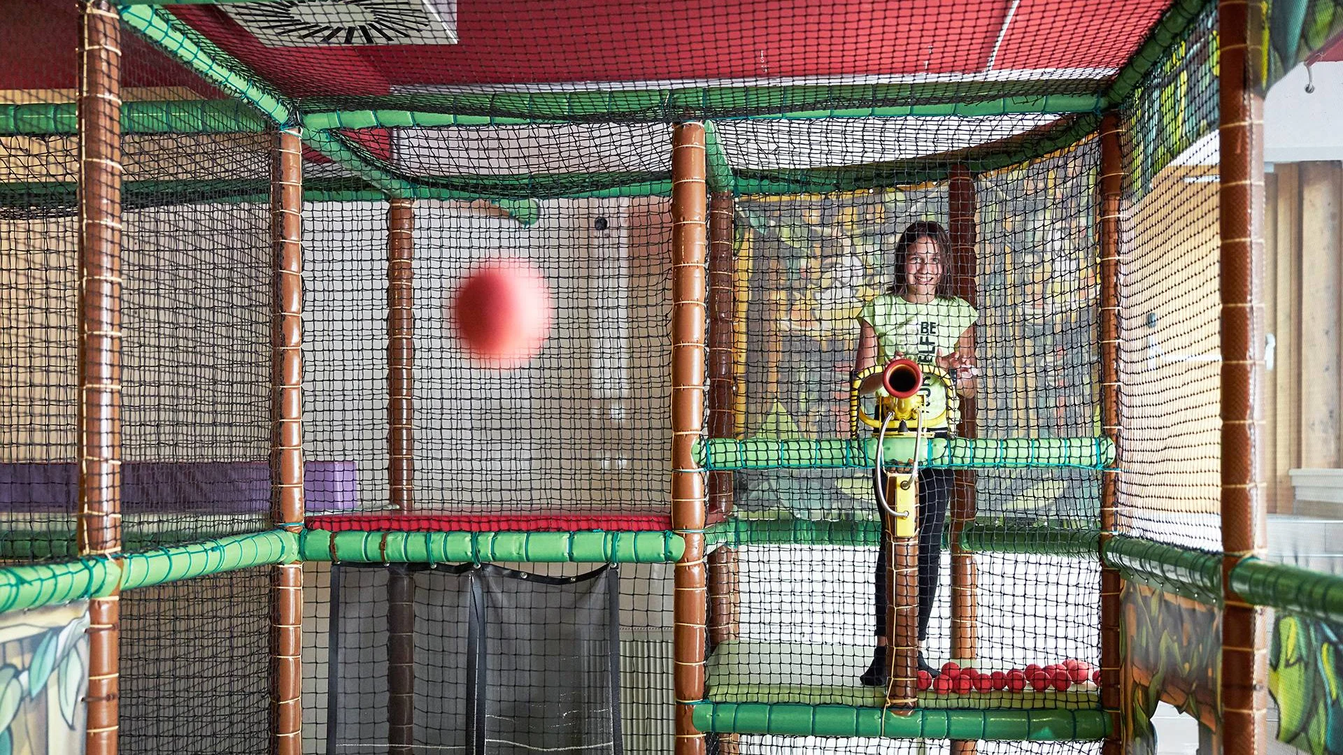 Mädchen spielt mit Bällen in einem Indoor-Spielplatz mit Netzwänden