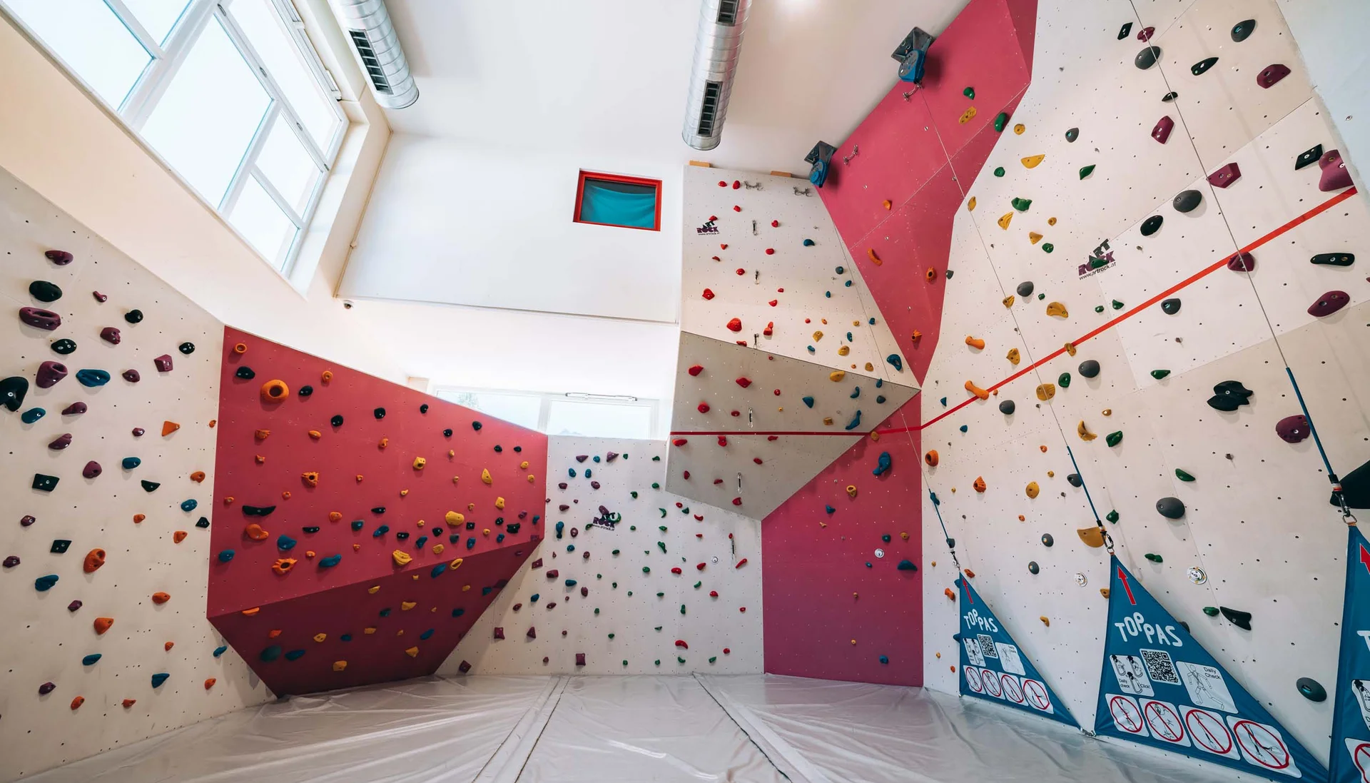 Innenansicht einer Kletterhalle mit bunten Griffen und Matten am Boden