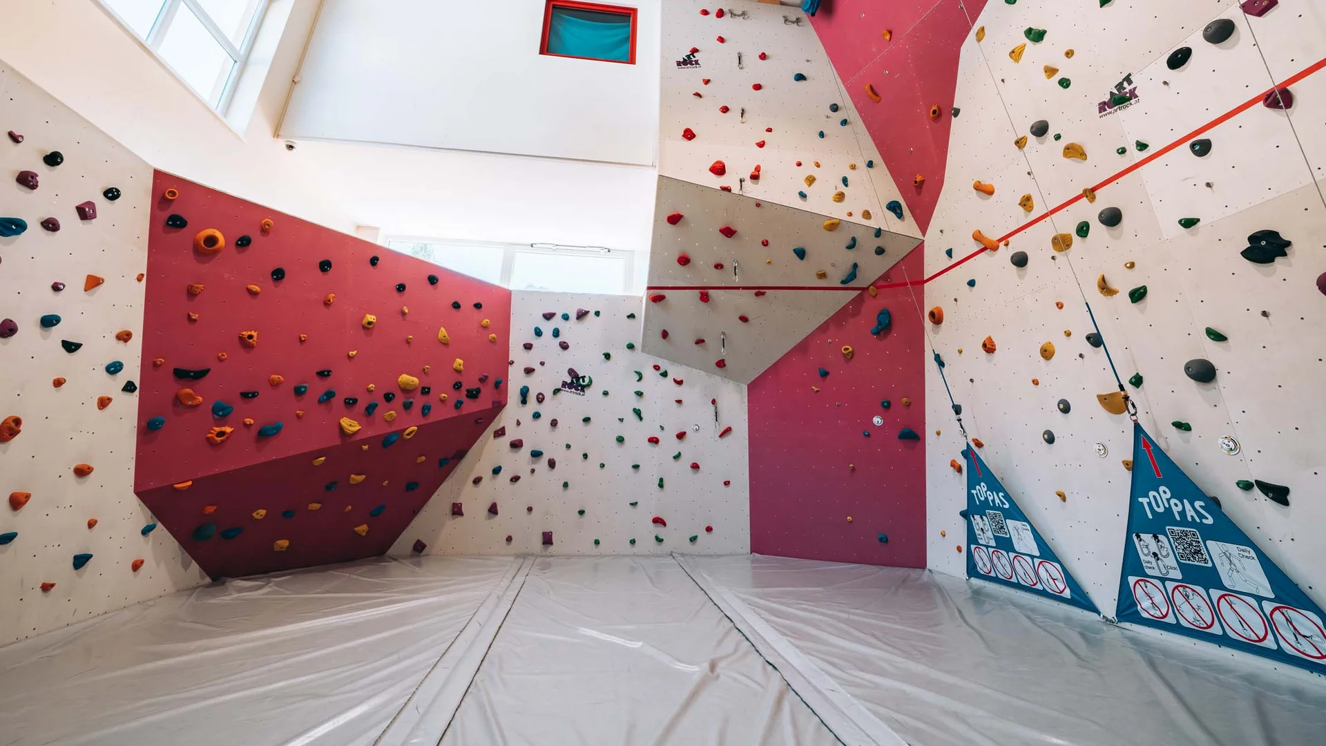 Innenansicht einer Kletterhalle mit bunten Griffen und Matten am Boden