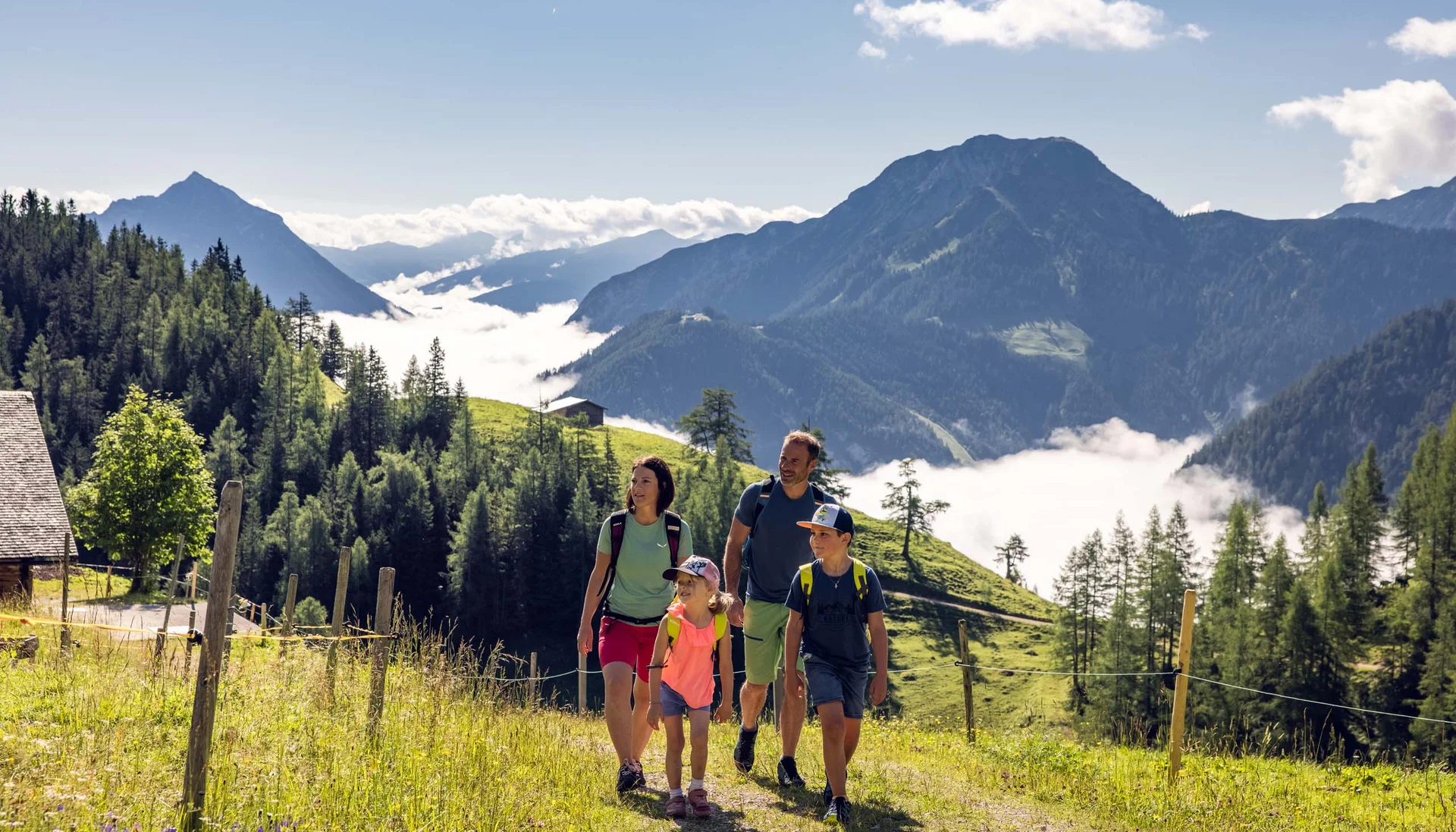 Familie wandert auf Bergweg mit Alpenlandschaft und Nebel im Tal