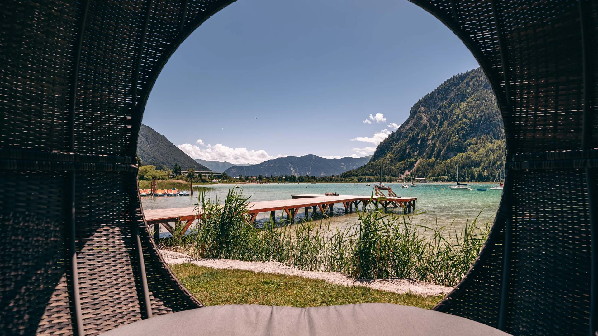 Blick auf einen Steg und Berge durch eine runde Öffnung eines Korbs