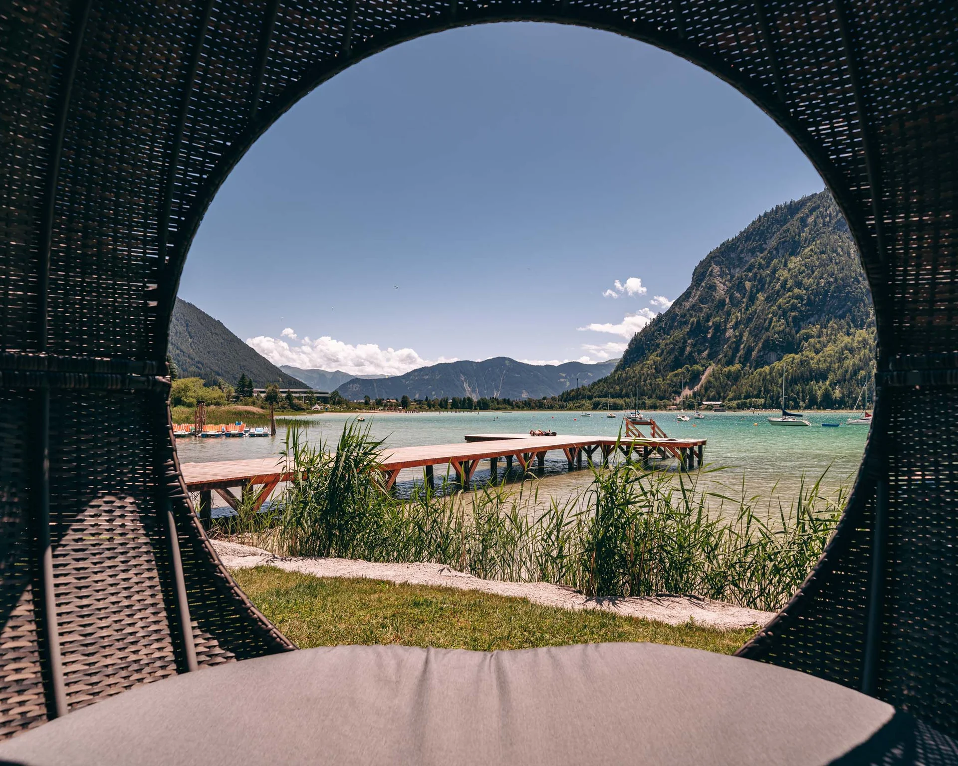 Blick auf einen Steg und Berge durch eine runde Öffnung eines Korbs