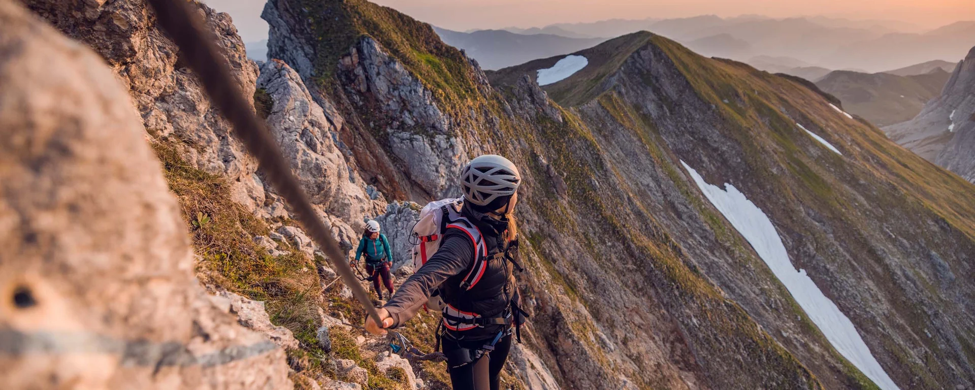 Kletterer sichert sich am Berggrat mit Seil bei Sonnenuntergang