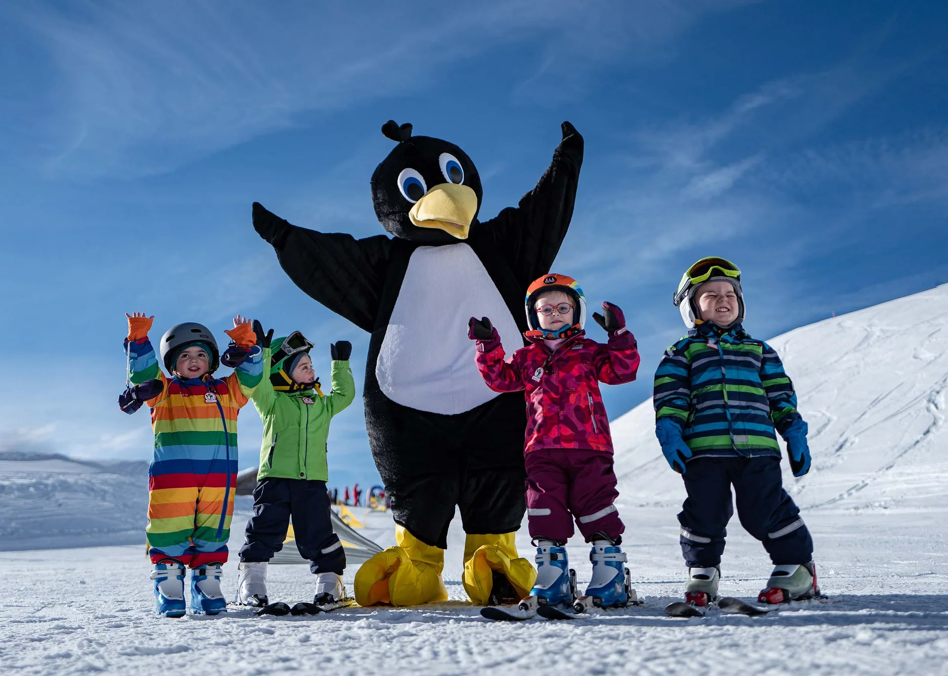 Kinder mit Skiausrüstung posieren neben einer Person im Pinguin-Kostüm im Schnee