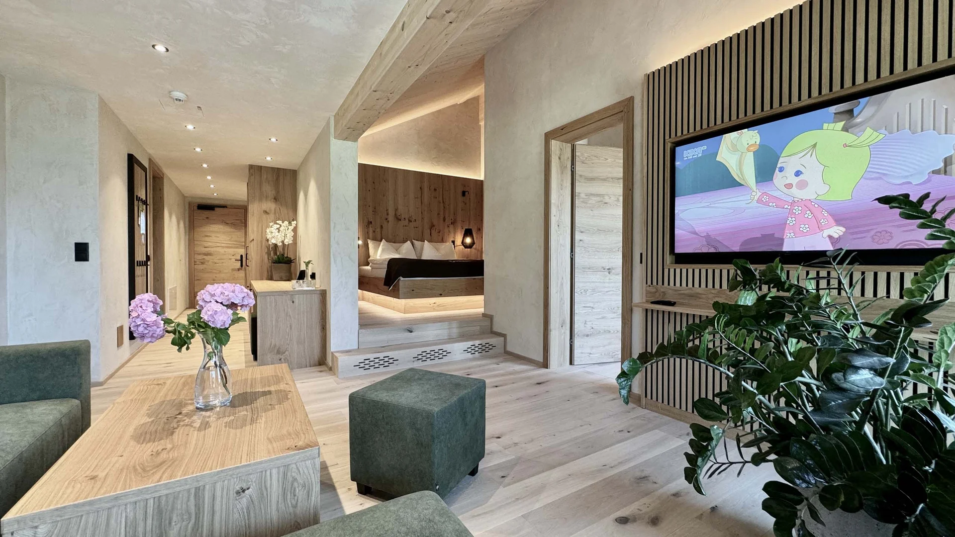 Moderner Hotelwohnraum mit grünem Sofa, TV und Schlafzimmer im Hintergrund