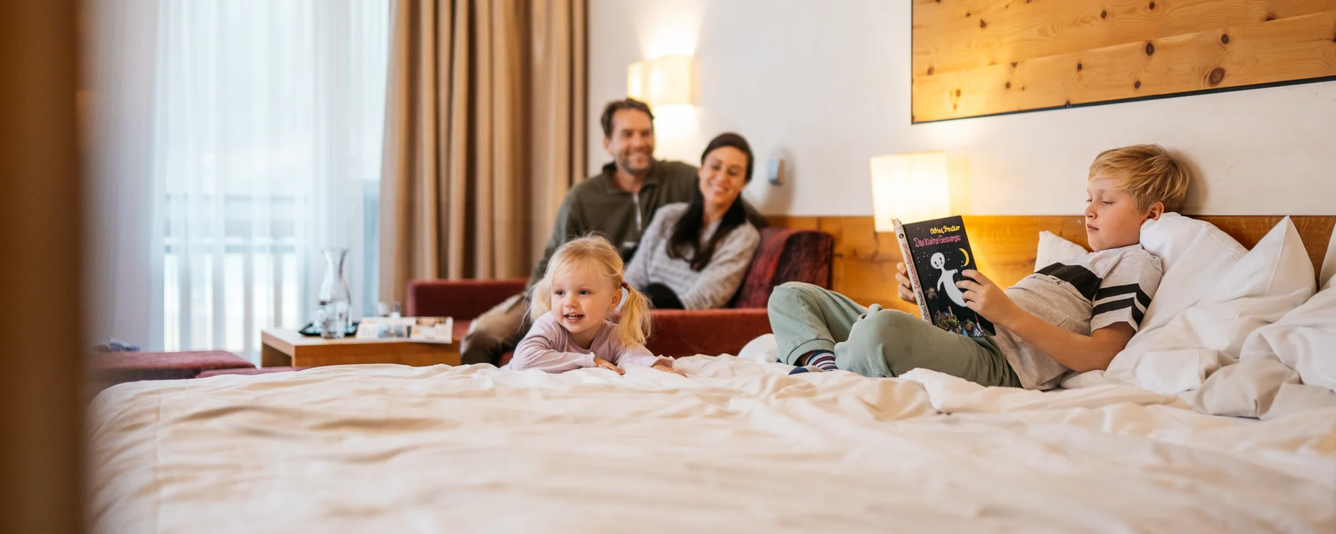 Familie entspannt im Hotelzimmer, Kind liest Buch auf dem Bett