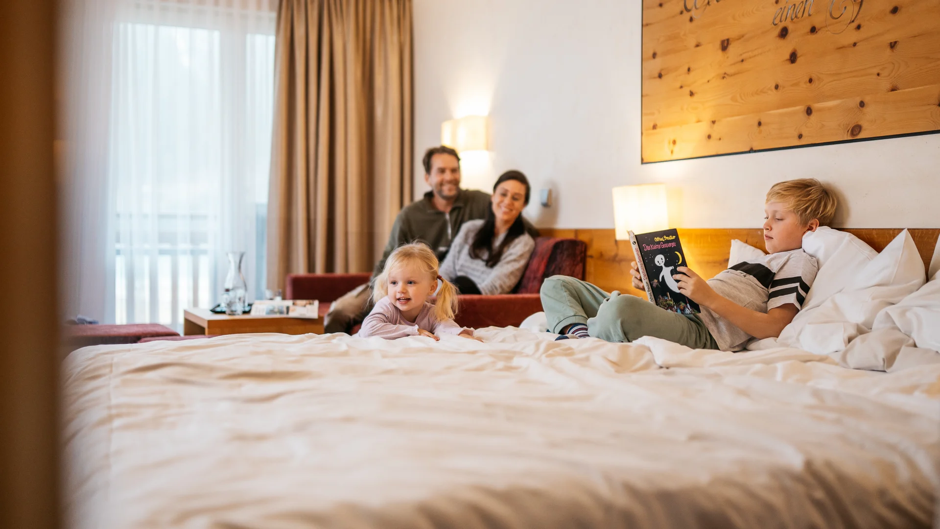 Familie entspannt im Hotelzimmer, Kind liest Buch auf dem Bett