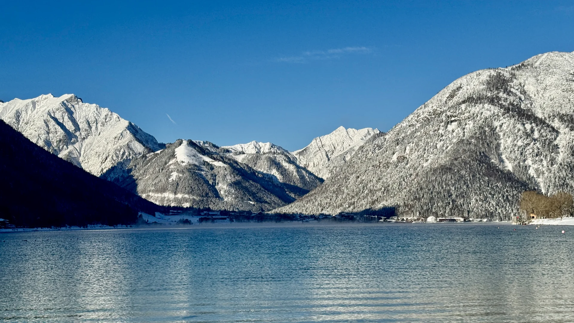 Schneebedeckte Berge spiegeln sich im ruhigen Bergsee unter blauem Himmel