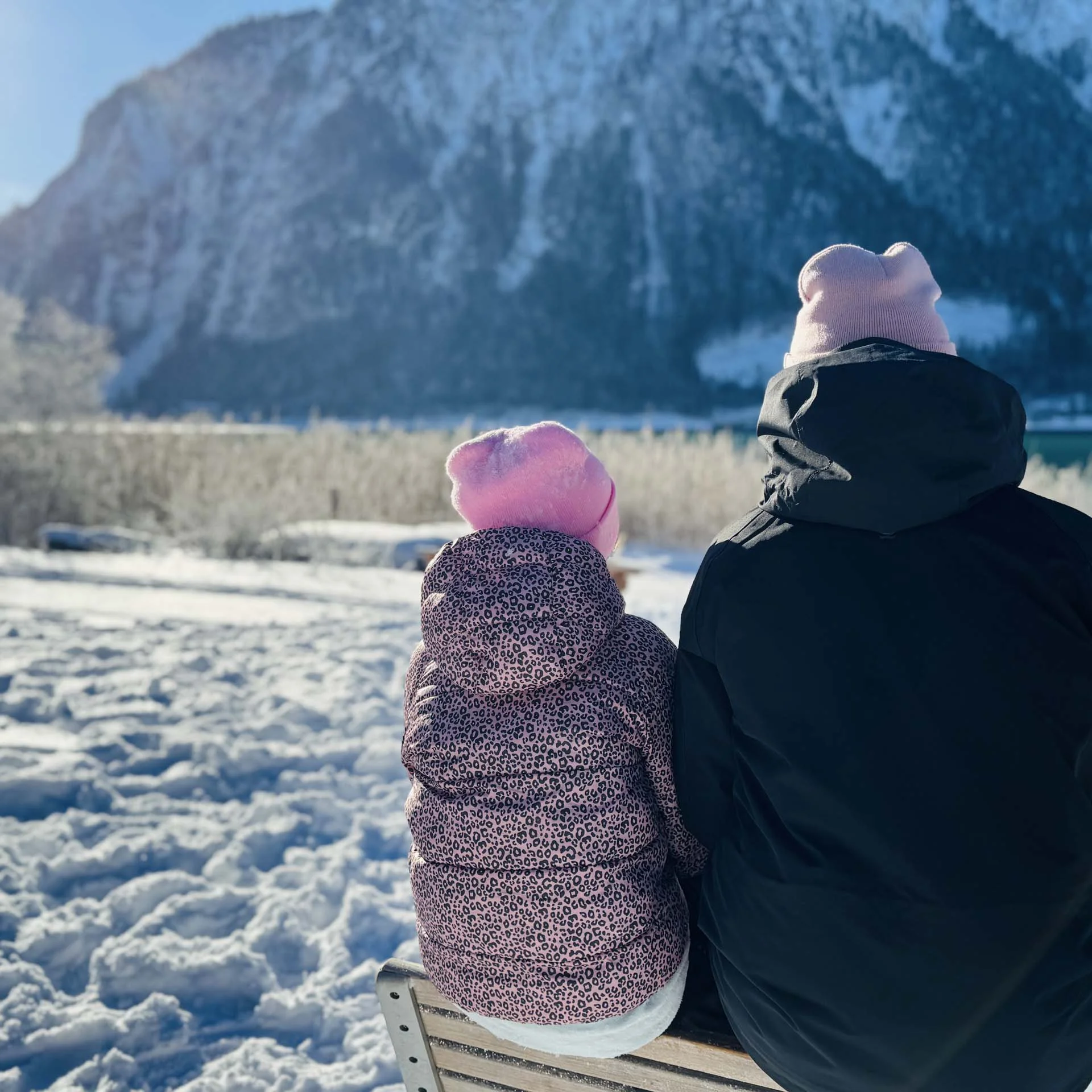 Familienzeit im Kinderhotel Buchau am Achensee Zwei Personen mit Mützen sitzen im Schnee und blicken auf verschneite Berge