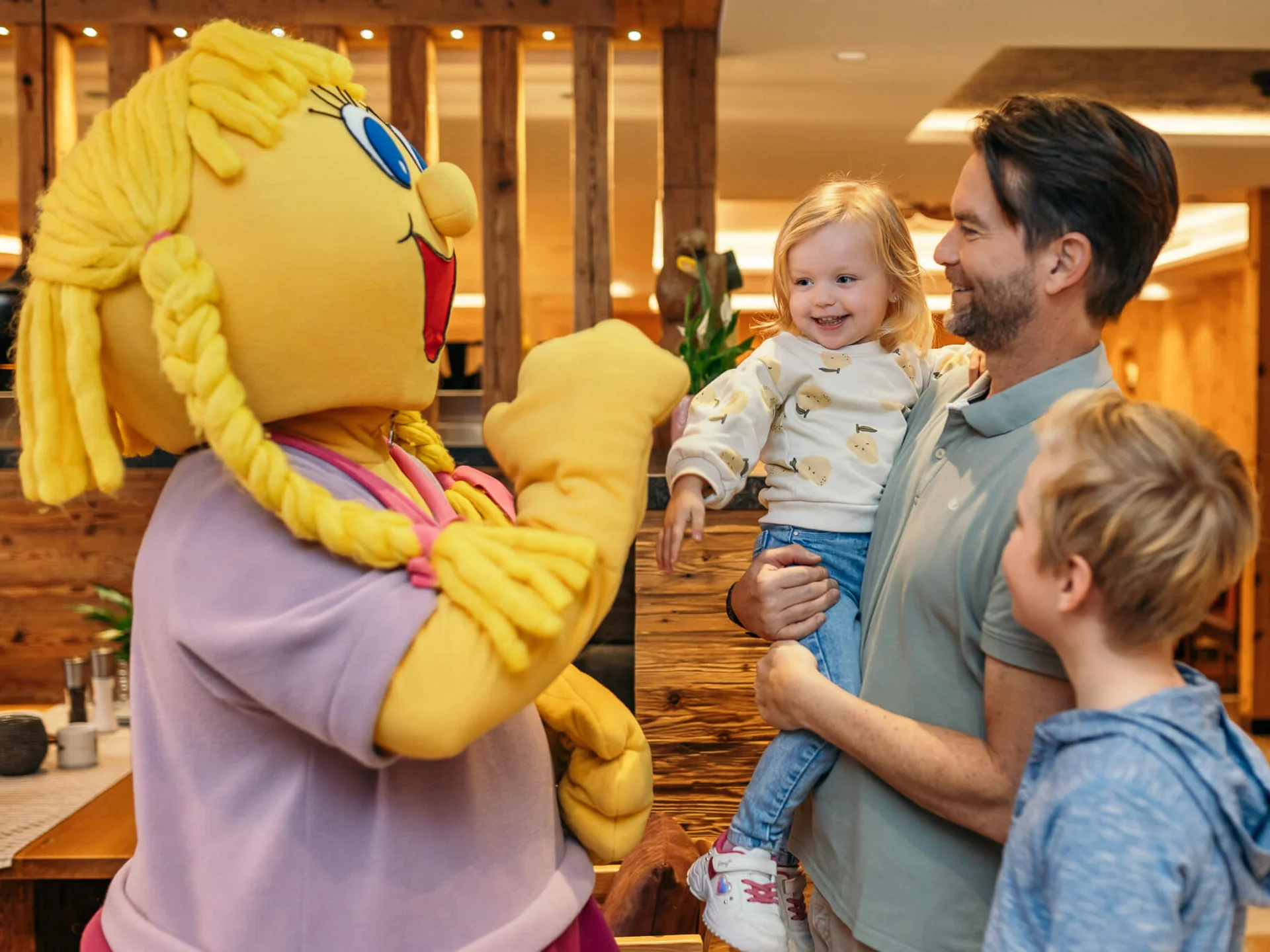Kind lacht, während es mit einem gelben Maskottchen im Restaurant interagiert