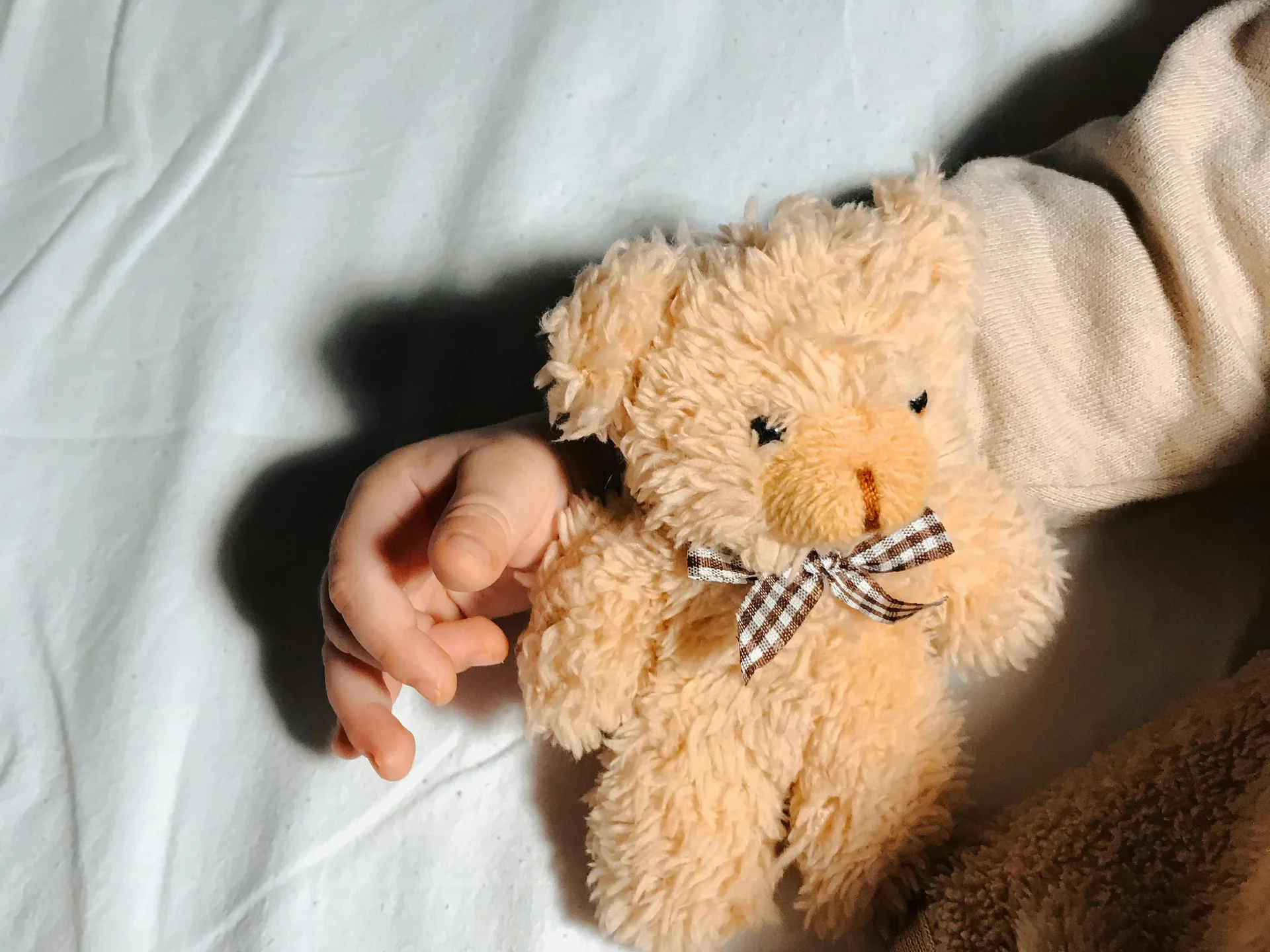 Hand holding small beige teddy bear with striped bow on white fabric