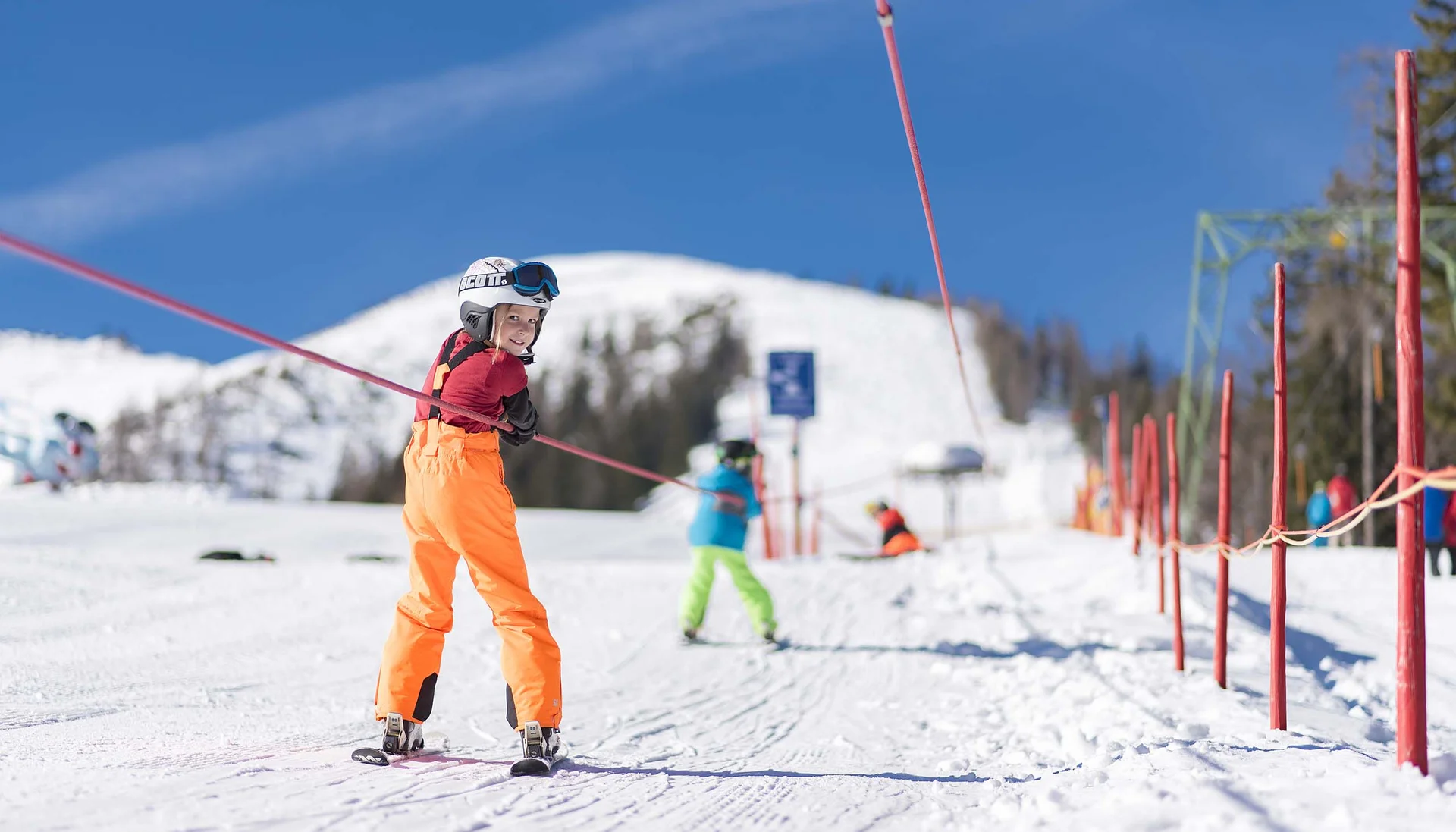 Kind in orange Skihose fährt an einem Skilift am sonnigen Schneehang