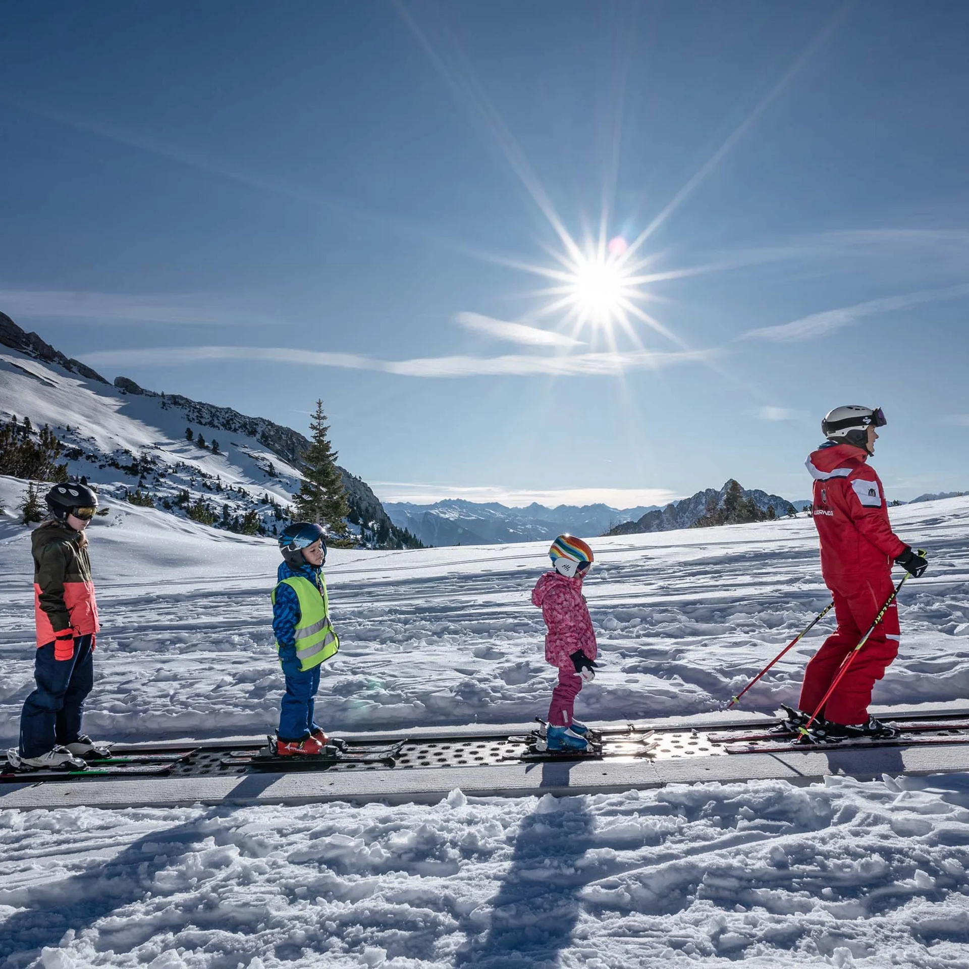 Kinder und Skilehrer auf Förderband im Skigebiet bei sonnigem Winterwetter
