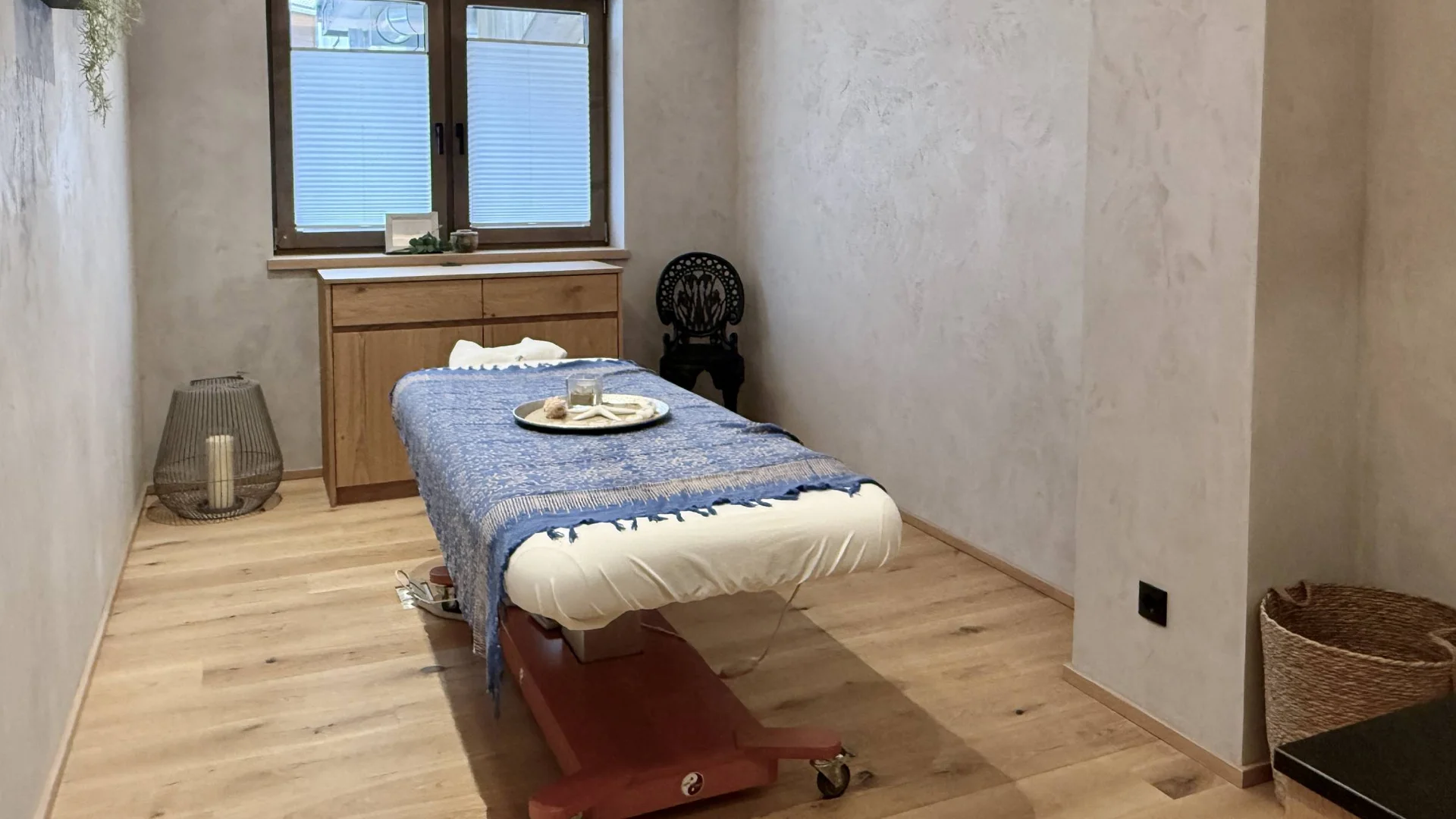 Sanfter Massageraum mit Behandlungsbett, Holzmöbeln und entspannender Dekoration