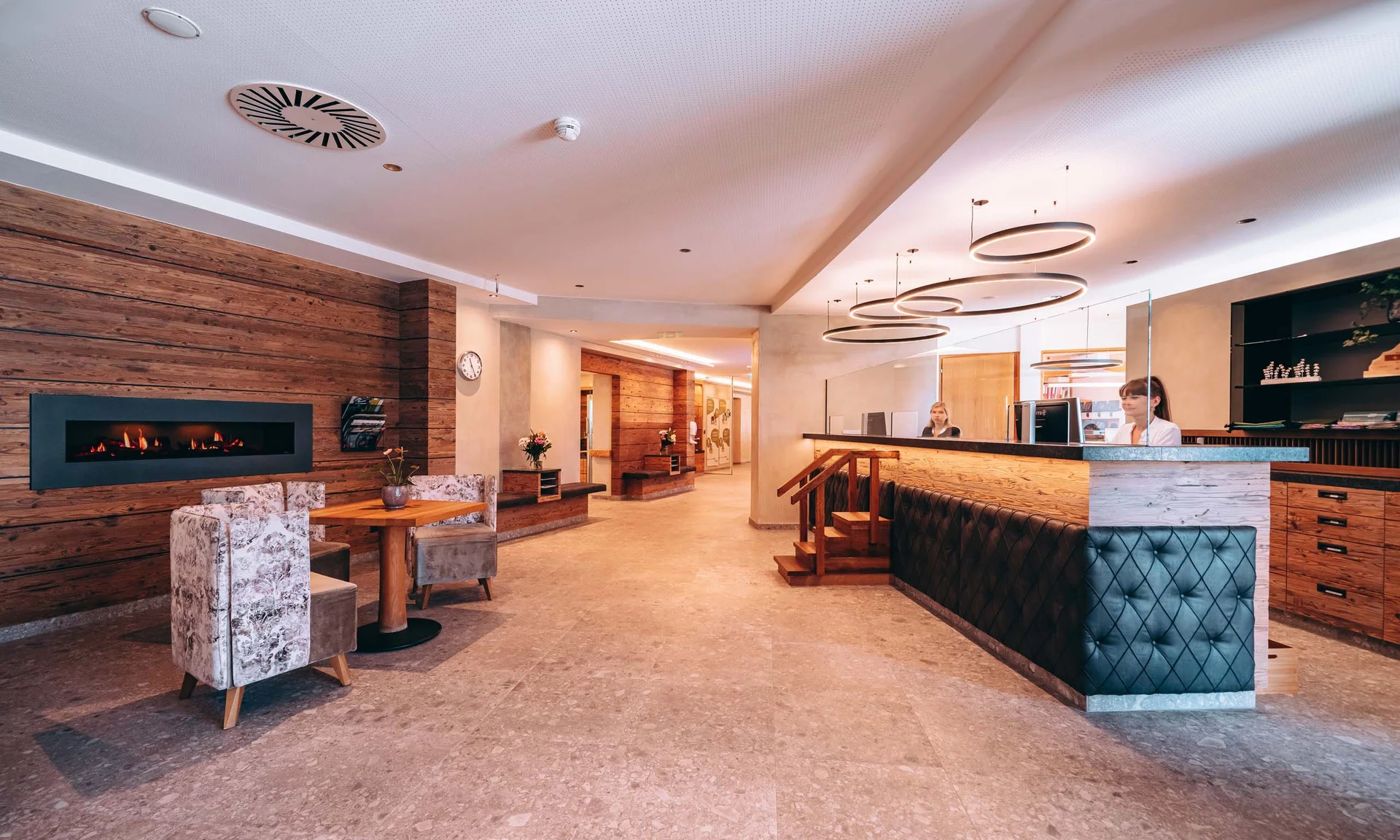 Moderner Hotellobby mit Rezeption, Sitzbereich und Kamin an Holzwand