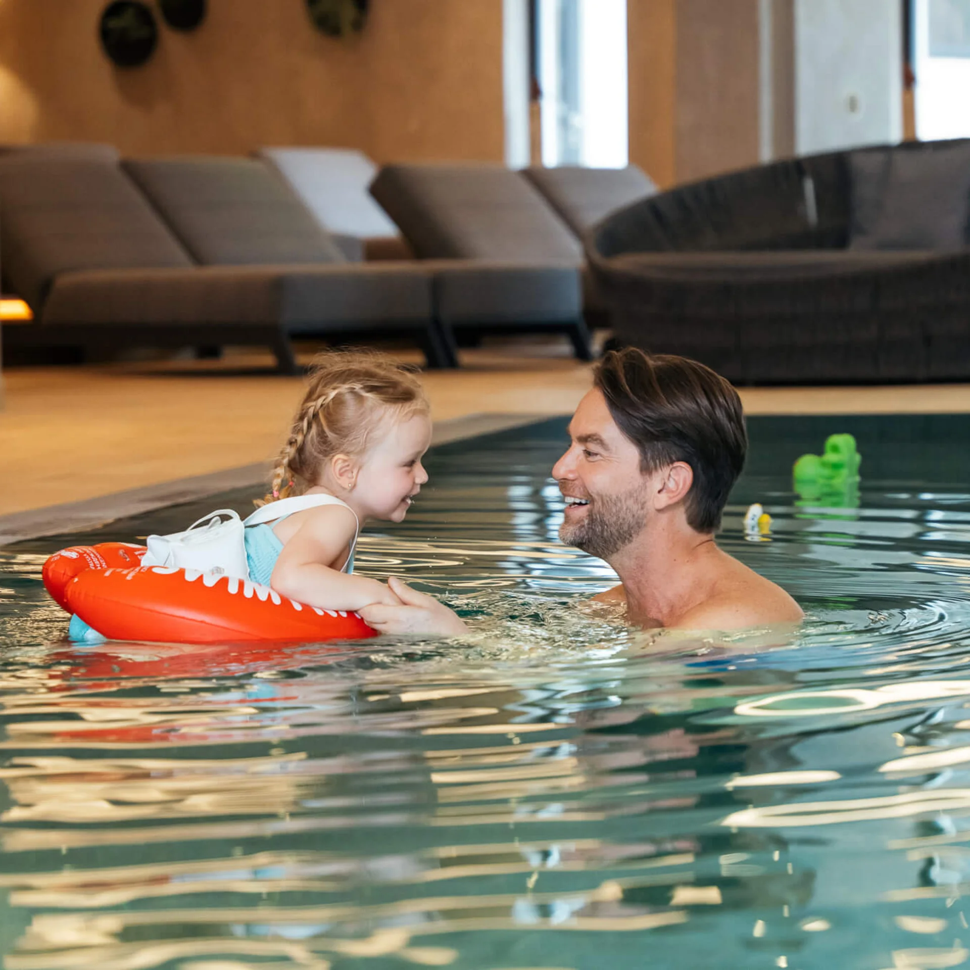 Vater und Tochter spielen lachend im Hallenbad zusammen