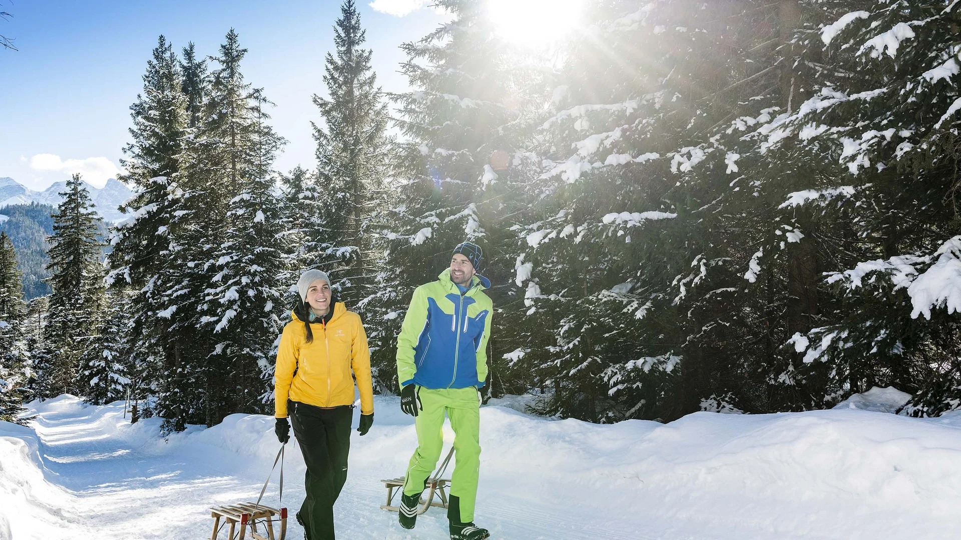 Ihr abenteuerlicher Erlebnisurlaub in Österreich Paar spaziert mit Schlitten auf schneebedecktem Waldweg bei Sonnenlicht
