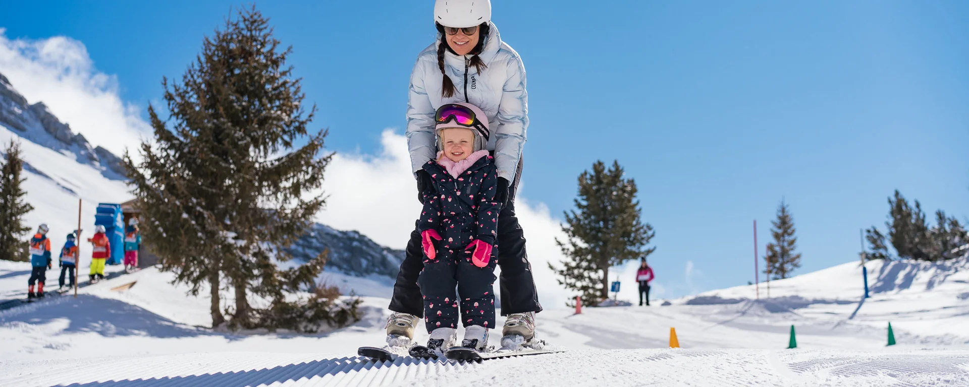 Outdoorspaß im Familienhotel am See in Österreich Erwachsene hilft kleinem Kind beim Skifahren auf verschneiter Piste