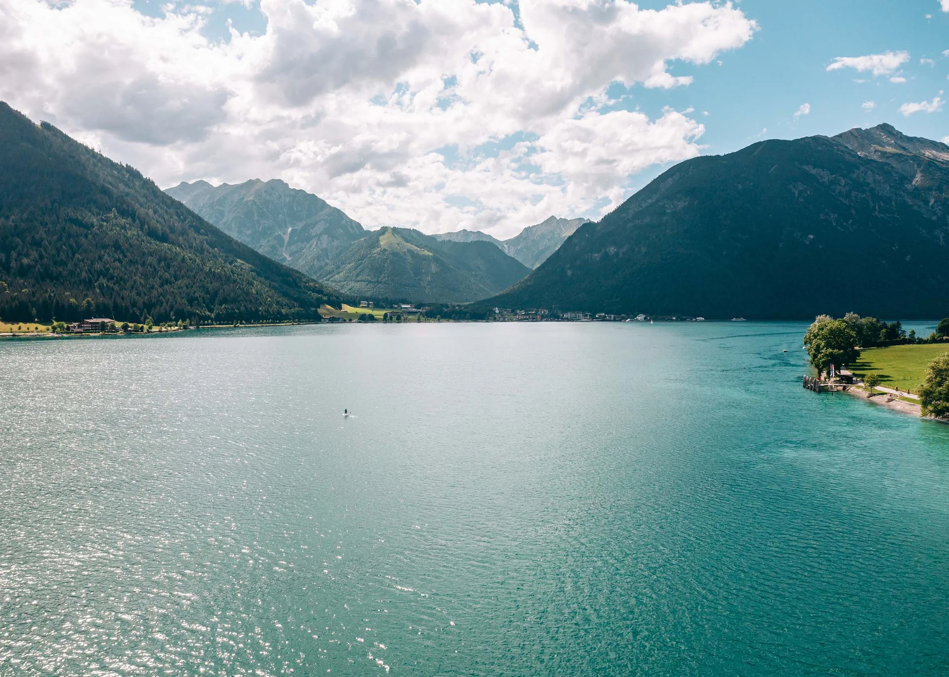 Blauer Bergsee umgeben von bewaldeten Bergen unter bewölktem Himmel