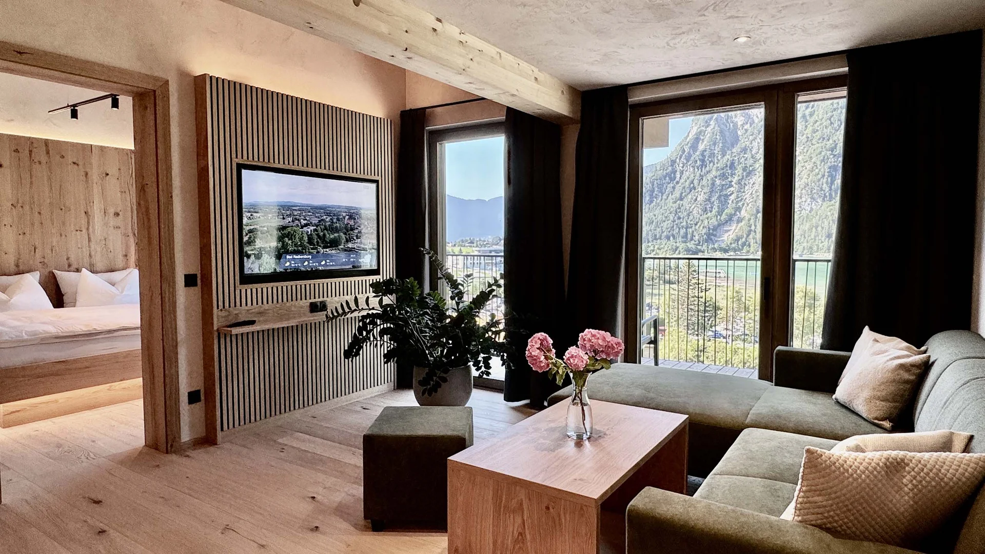 Modernes Wohnzimmer mit grüner Couch, Holzboden und Bergblick durch große Fenster