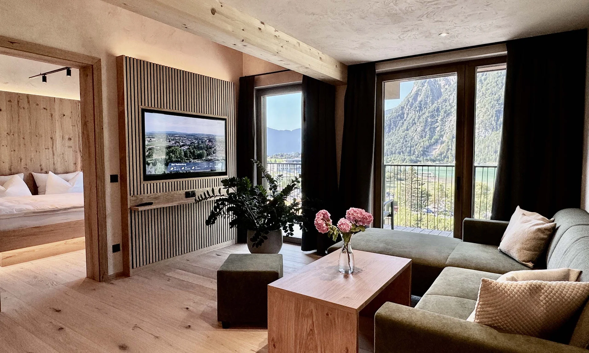 Modernes Wohnzimmer mit grüner Couch, Holzboden und Bergblick durch große Fenster