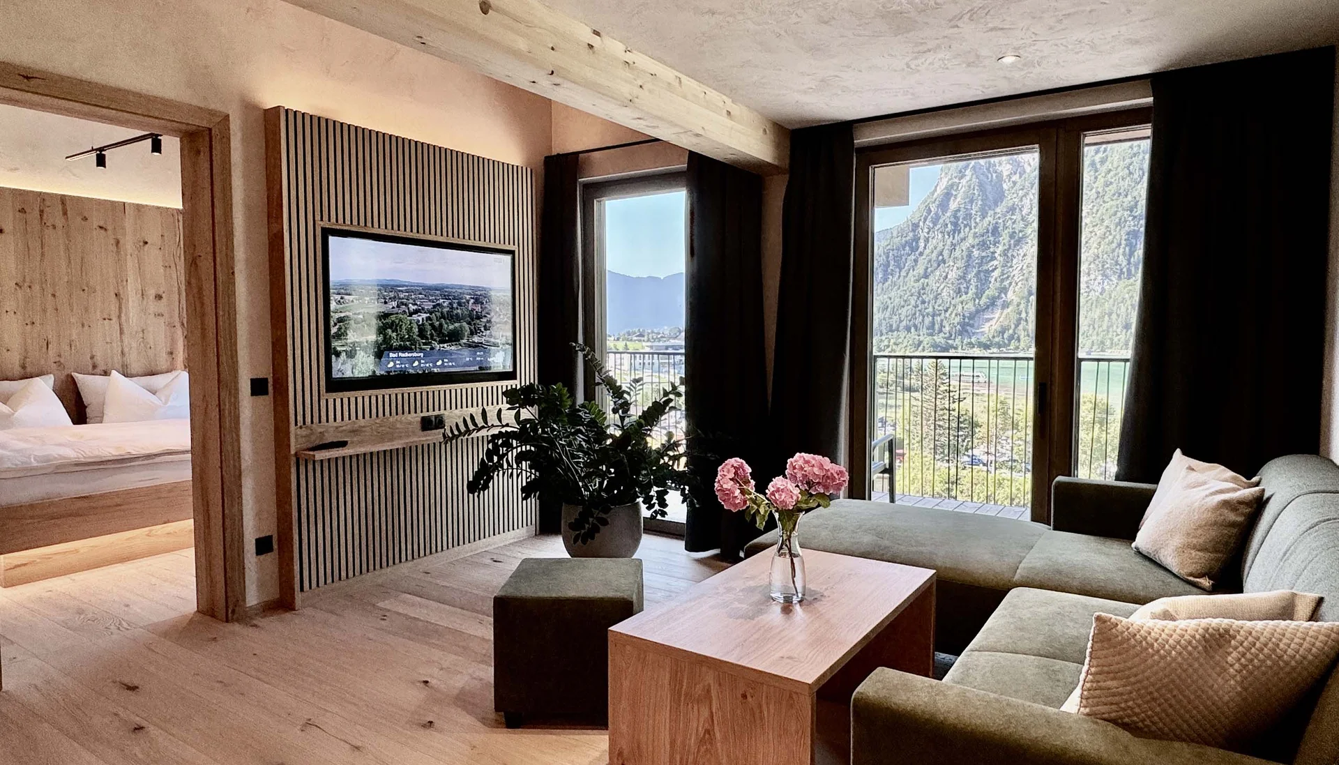 Modernes Wohnzimmer mit grüner Couch, Holzboden und Bergblick durch große Fenster