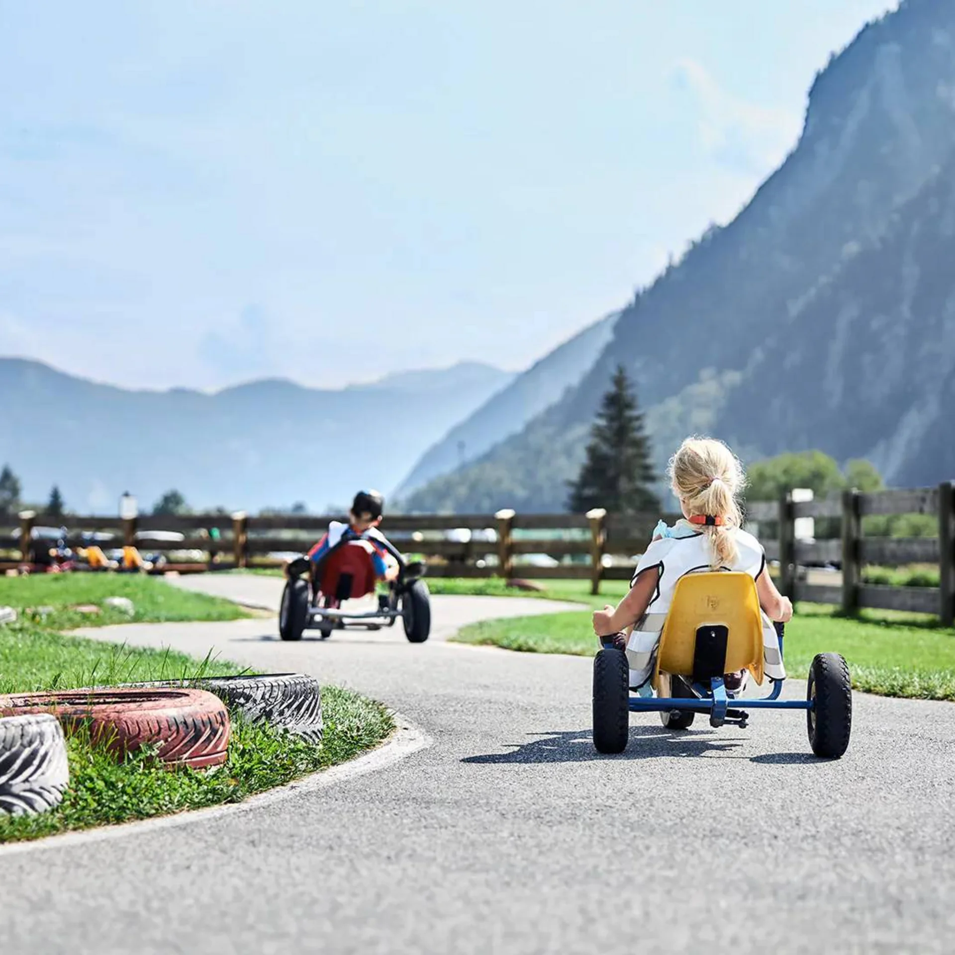 Kinder fahren Tretautos auf einer kurvigen Bahn in ländlicher Berglandschaft