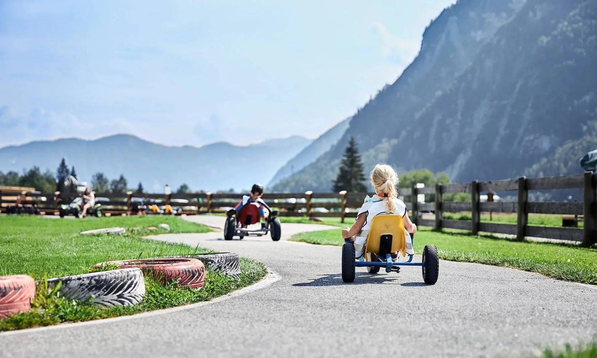 Kinder fahren Tretautos auf einer kurvigen Bahn in ländlicher Berglandschaft