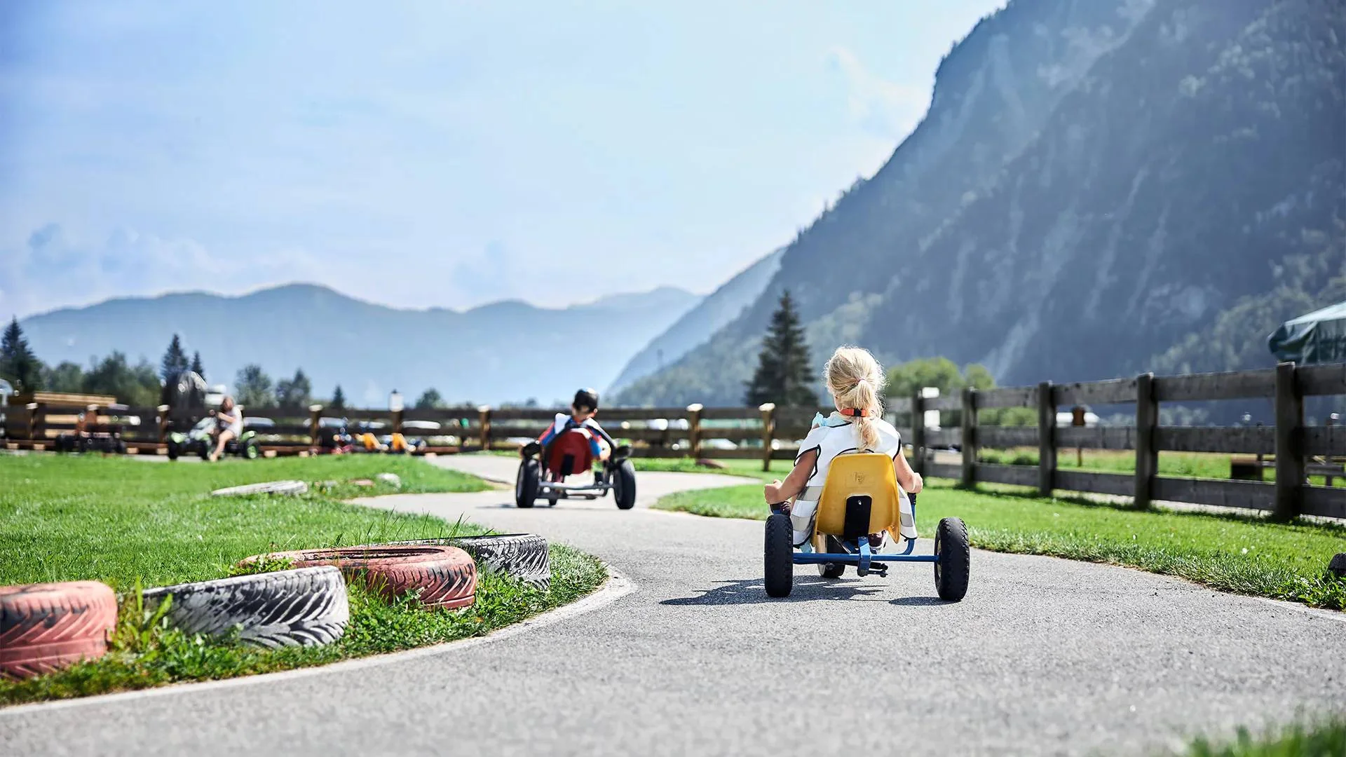 Kinder fahren Tretautos auf einer kurvigen Bahn in ländlicher Berglandschaft
