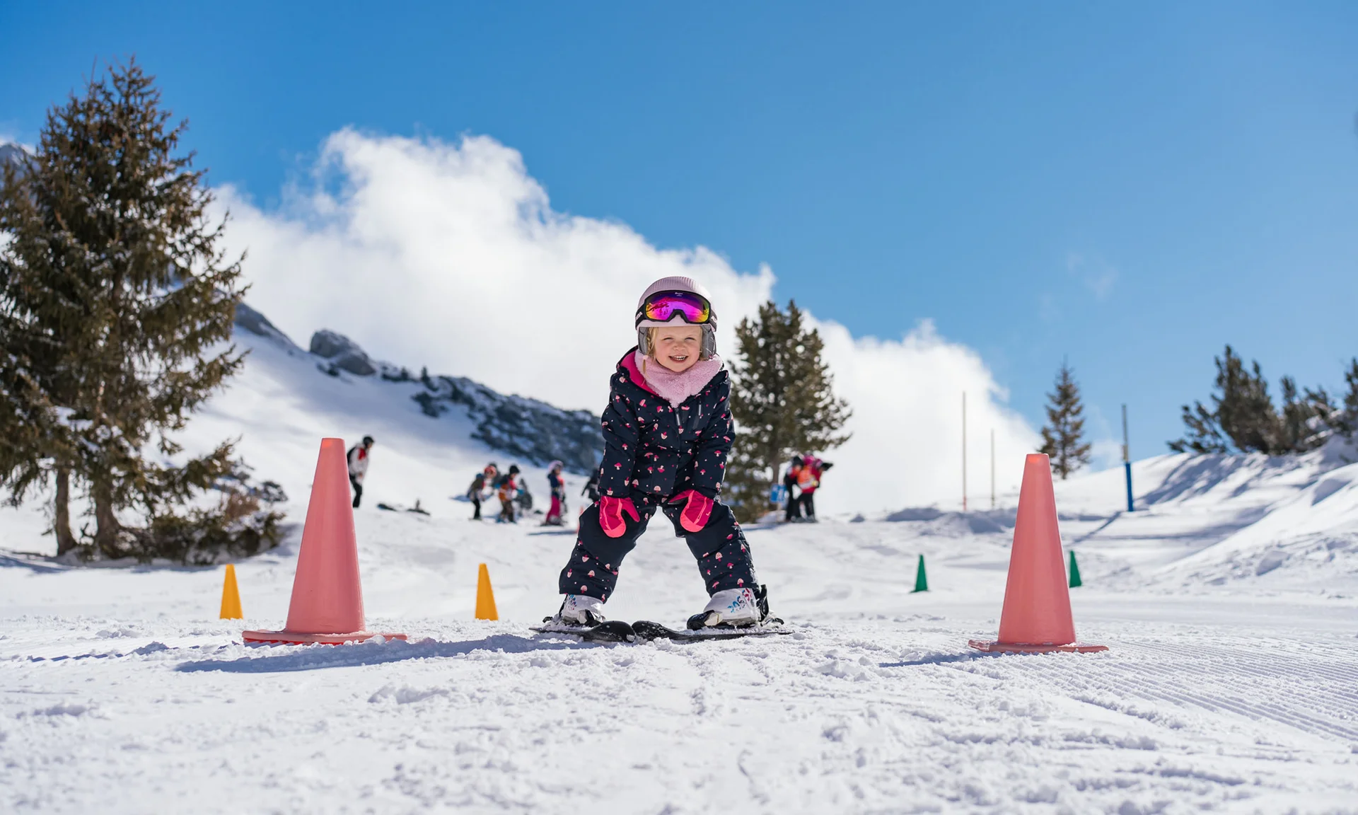 Child learning to ski between cones on snowy slope on a sunny day