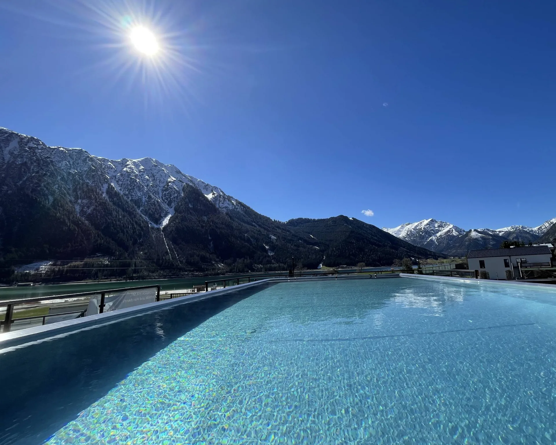 Blick auf einen Pool mit Berglandschaft und Sonnenschein bei klarem Himmel