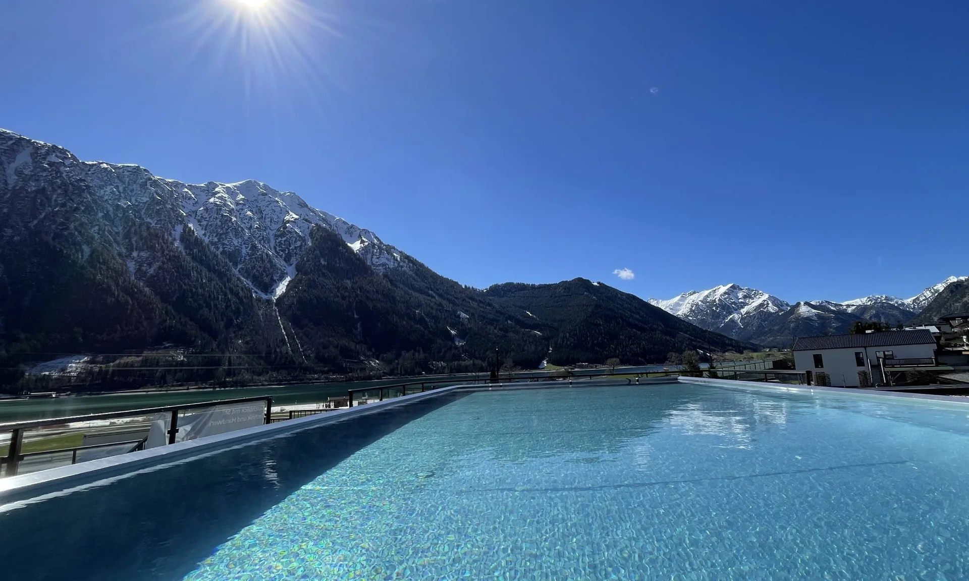 Blick auf einen Pool mit Berglandschaft und Sonnenschein bei klarem Himmel