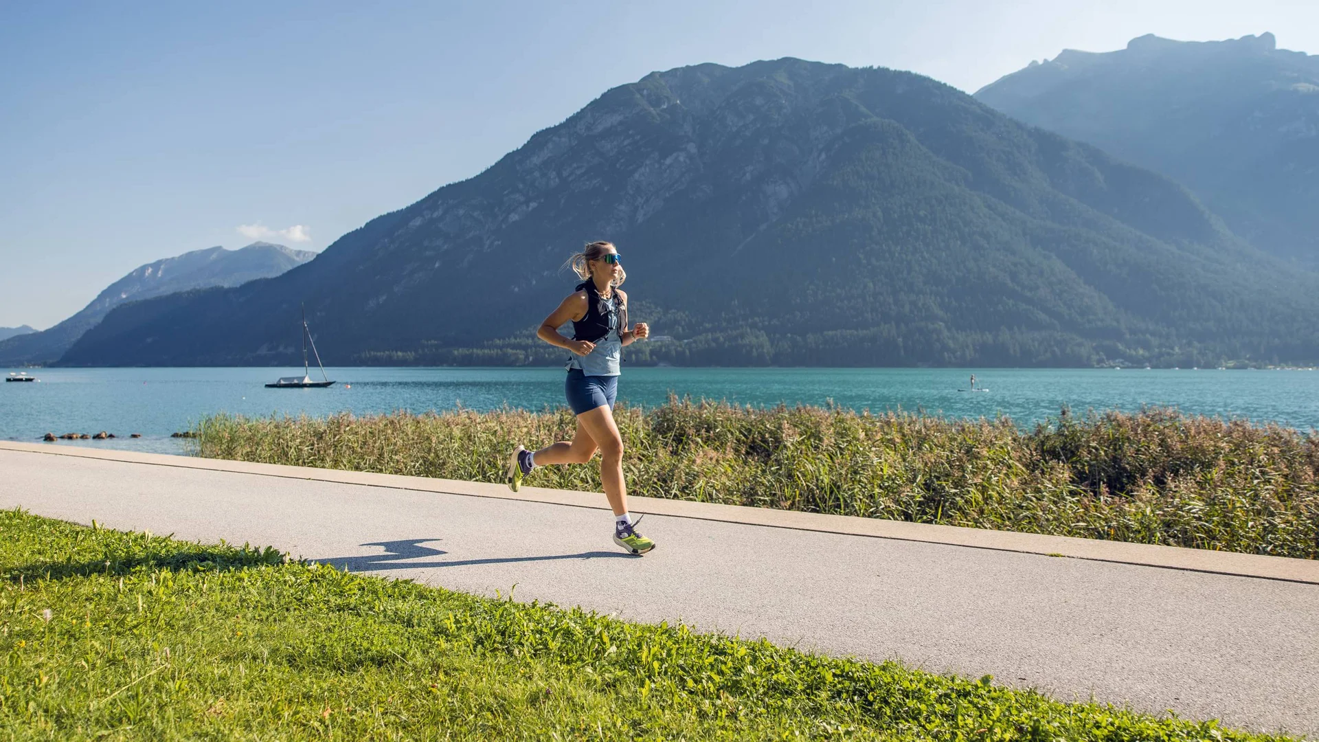 Frau joggt auf Weg am See mit Bergen im Hintergrund bei klarem Wetter