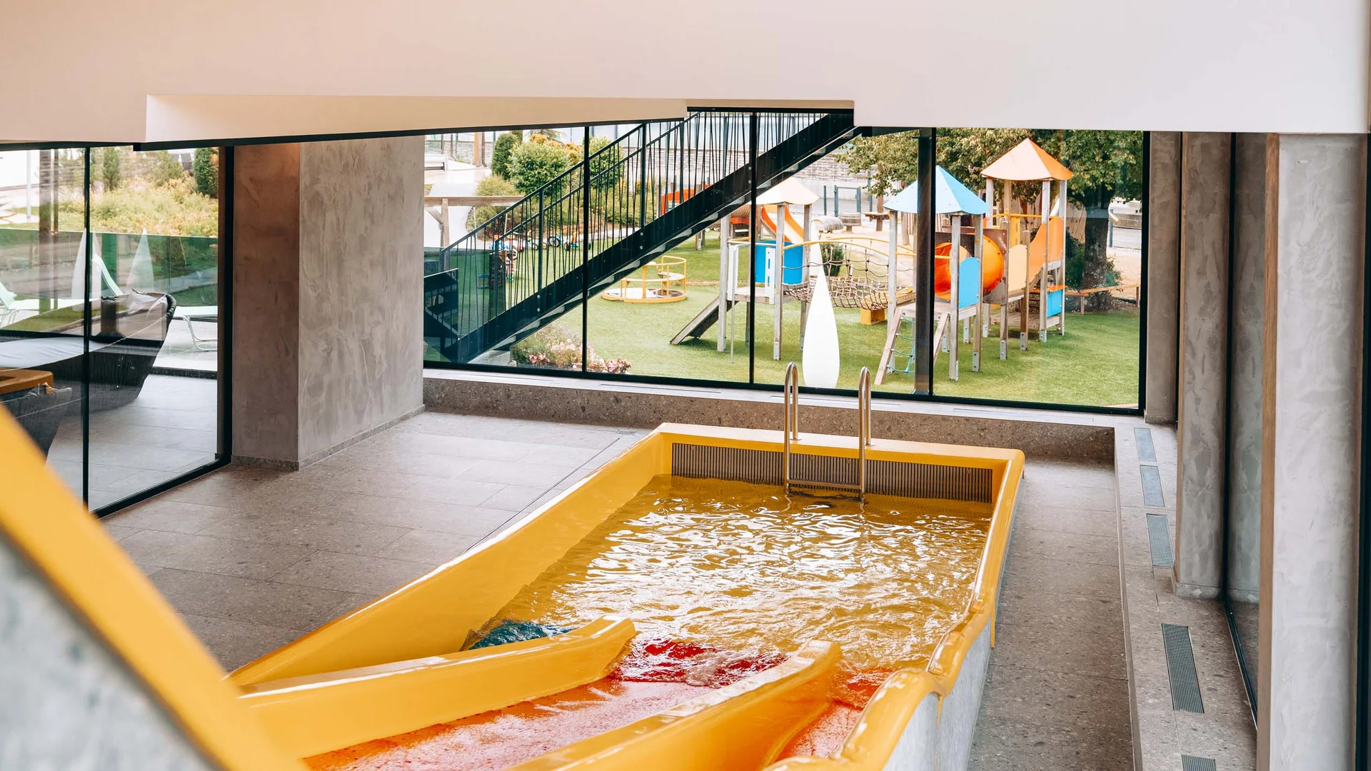 Gelbe Wasserrutsche in Innenbereich mit Blick auf Kinderspielplatz draußen