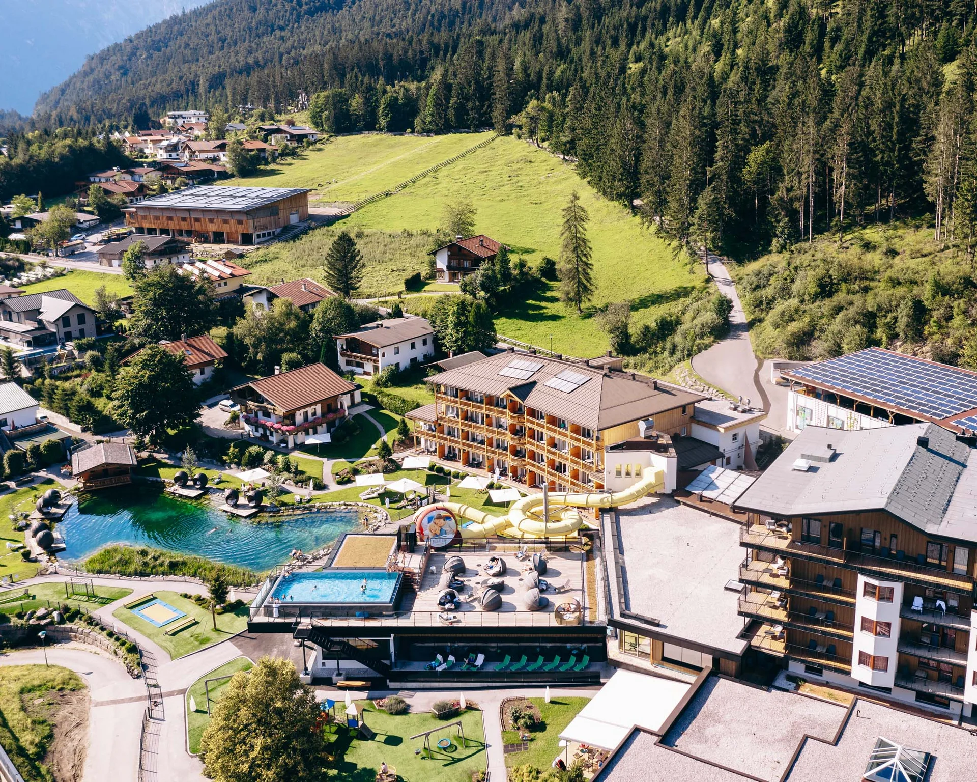 Luftaufnahme eines Resorts mit Schwimmbädern, Wasserrutsche und umgeben von Bergen