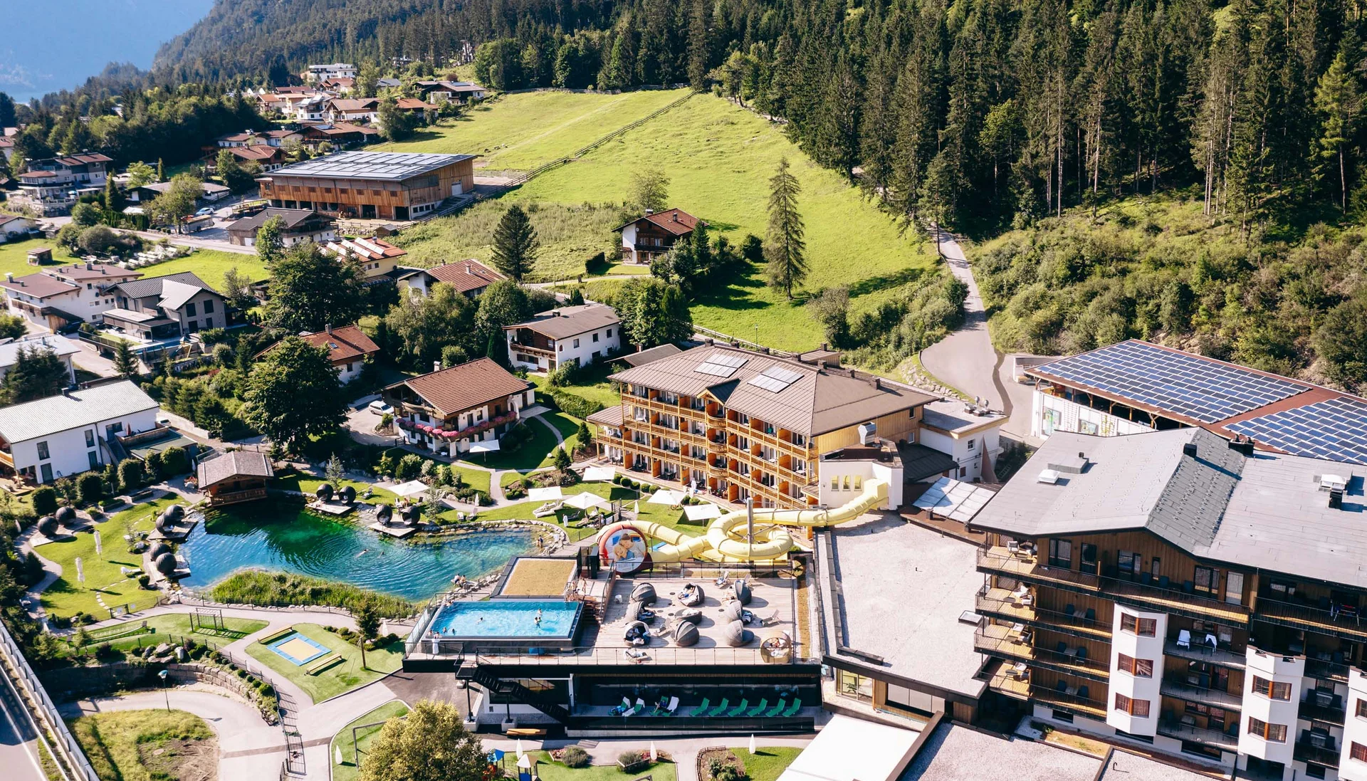 Aerial view of a resort with pools, water slide, and surrounded by mountains