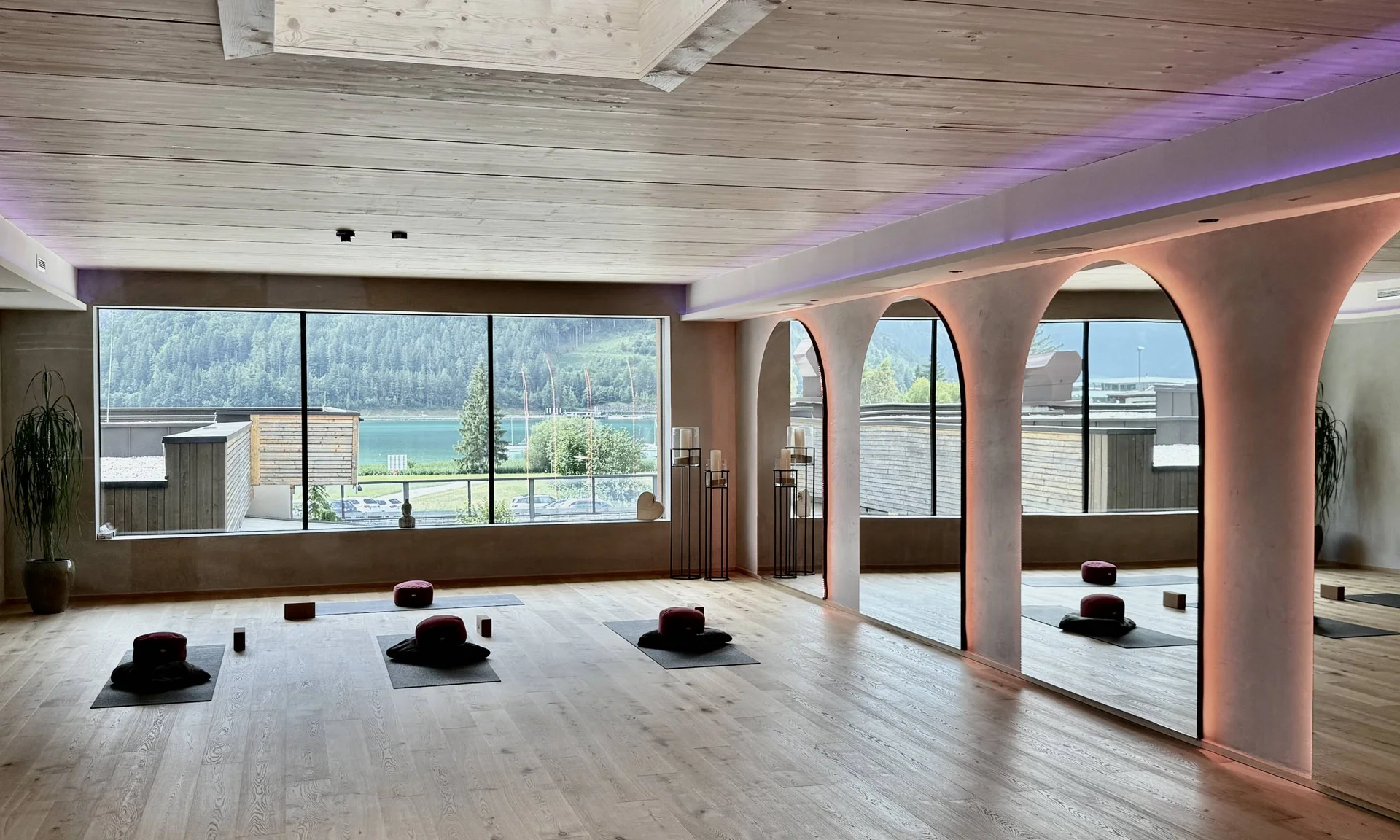 Helles Yoga-Studio mit Holzboden, Meditationskissen und großer Fensterfront mit Seeblick