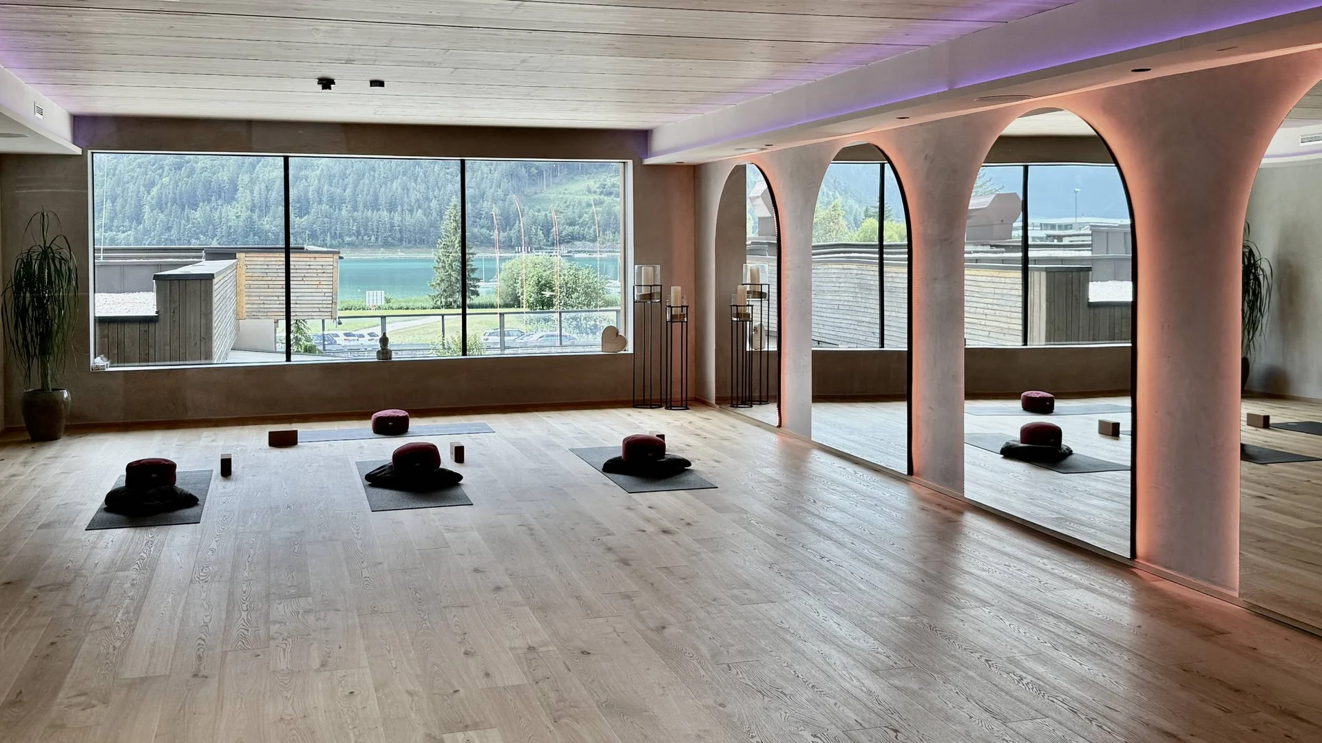 Helles Yoga-Studio mit Holzboden, Meditationskissen und großer Fensterfront mit Seeblick