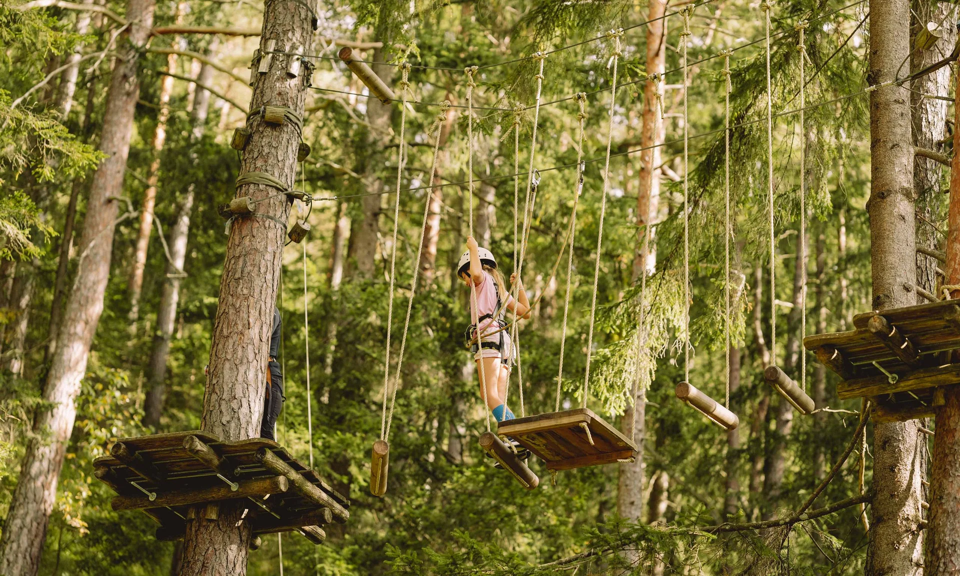 Kind mit Helm klettert im Hochseilgarten zwischen Bäumen