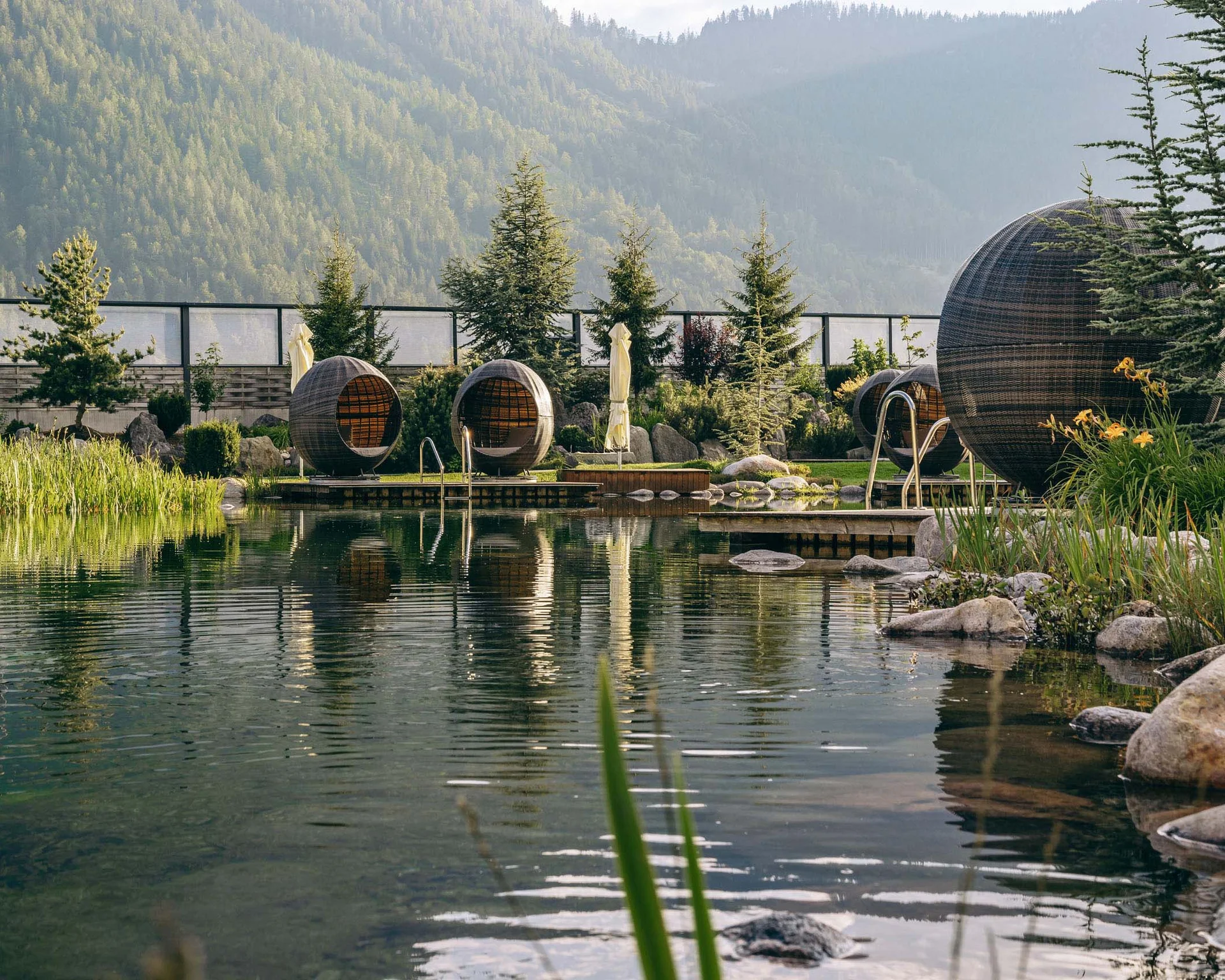 Natural pool with round seating pods in a garden area with mountains in the background