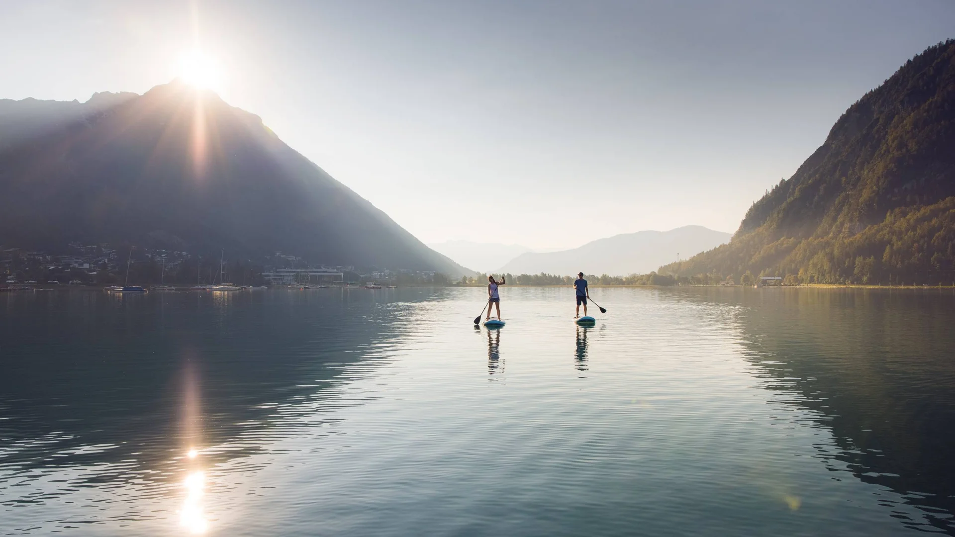 Zwei Personen paddleboarden auf ruhigem Bergsee bei Sonnenaufgang