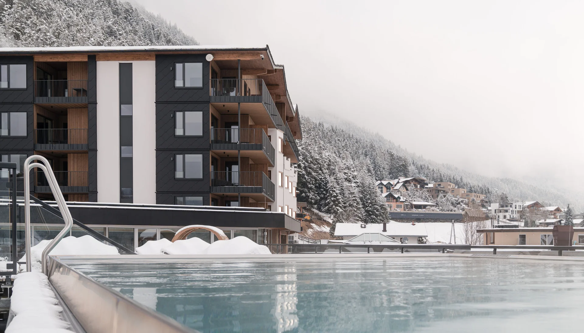 Erholungsurlaub für Eltern Beheiztes Außenbecken mit Blick auf verschneite Berge und Gebäude