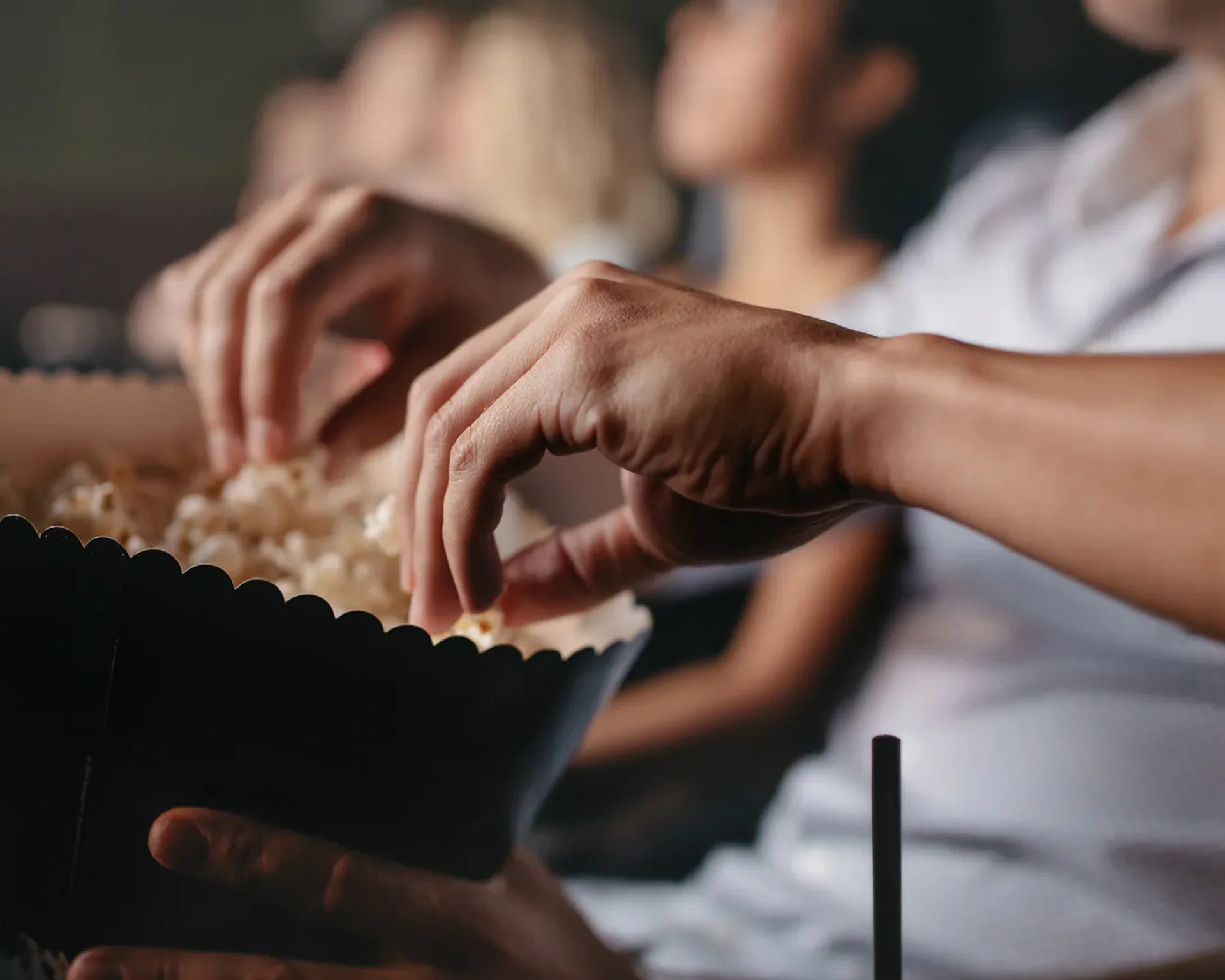 Person nimmt Popcorn aus einer großen Schüssel im Kino