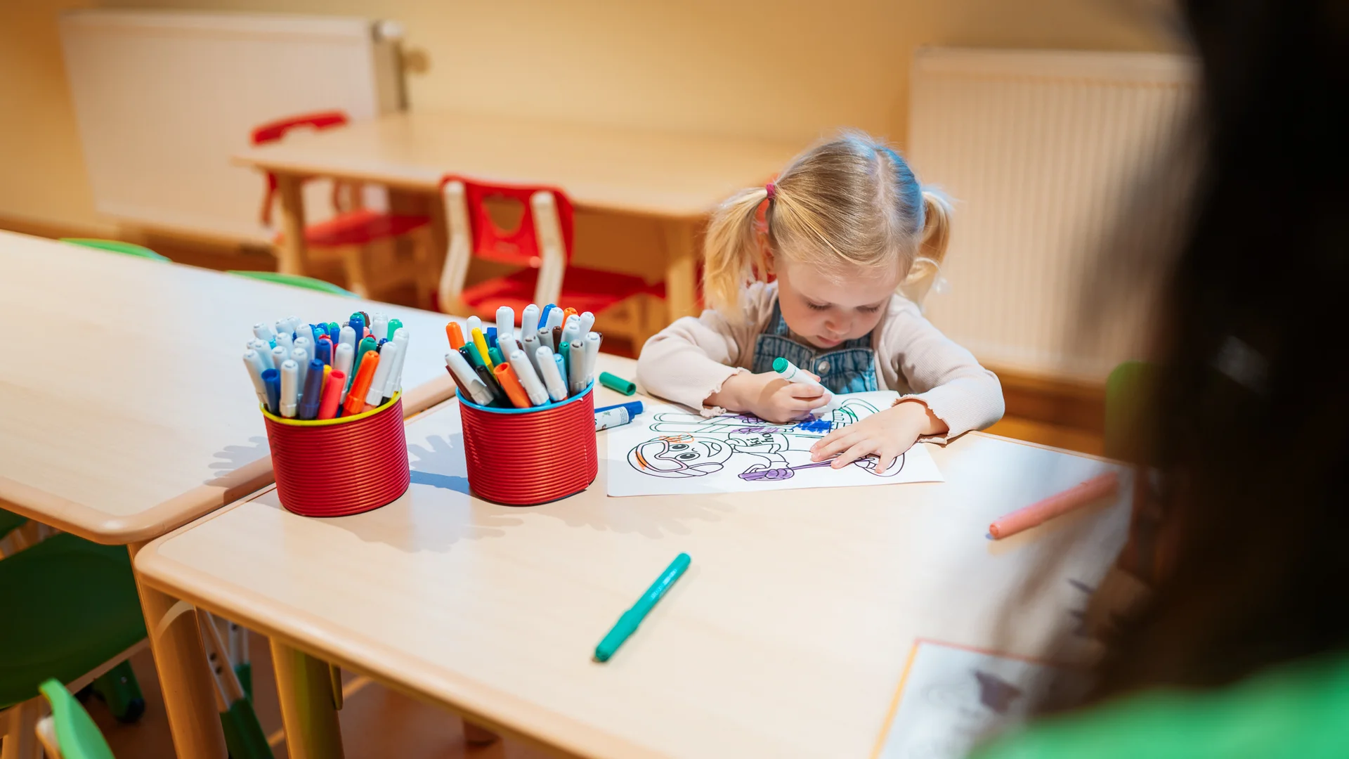 Kleines Mädchen malt mit Filzstift an einem Tisch in einem Klassenzimmer