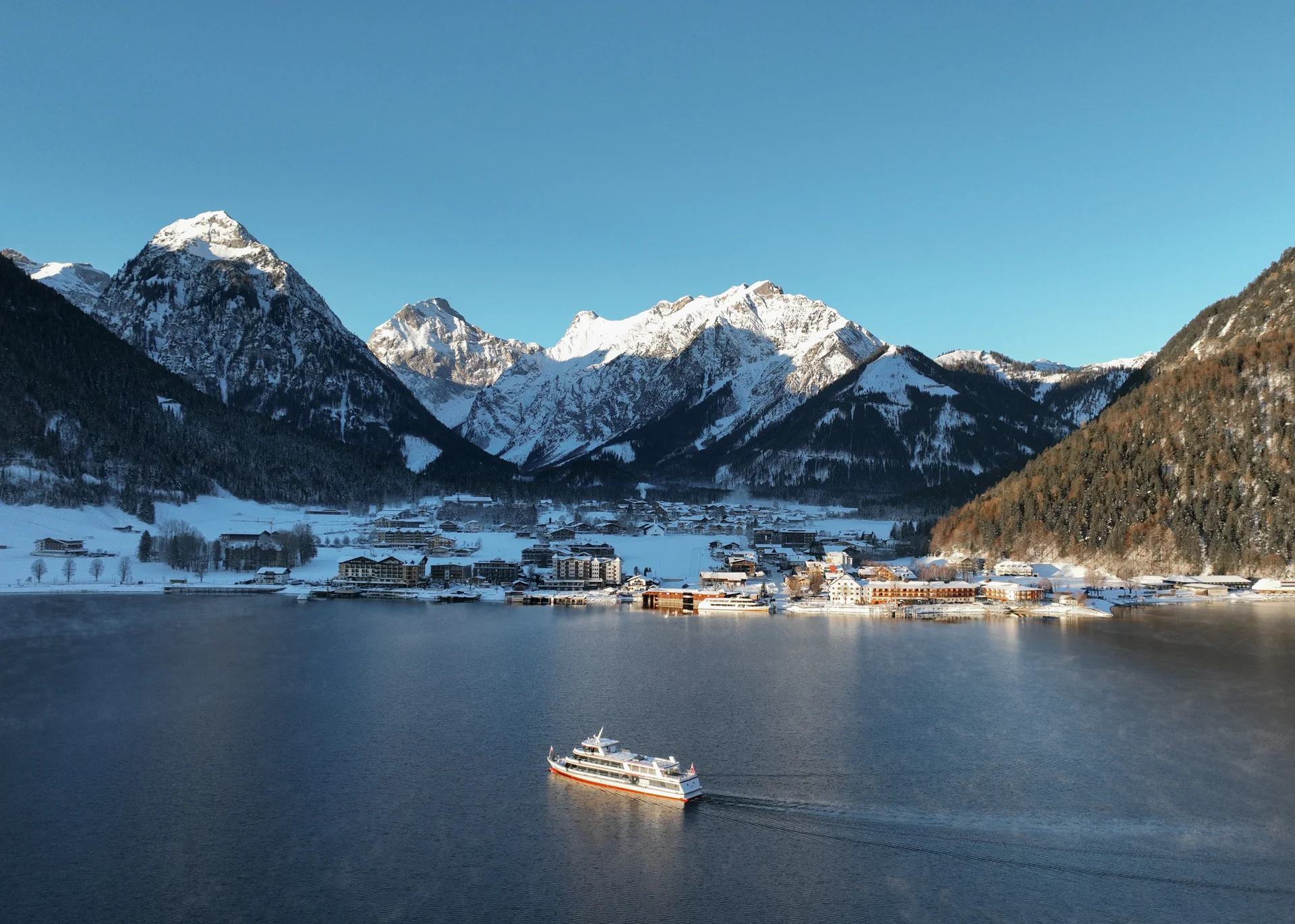 Schiff auf See vor schneebedecktem Bergdorf in klarer Winterlandschaft