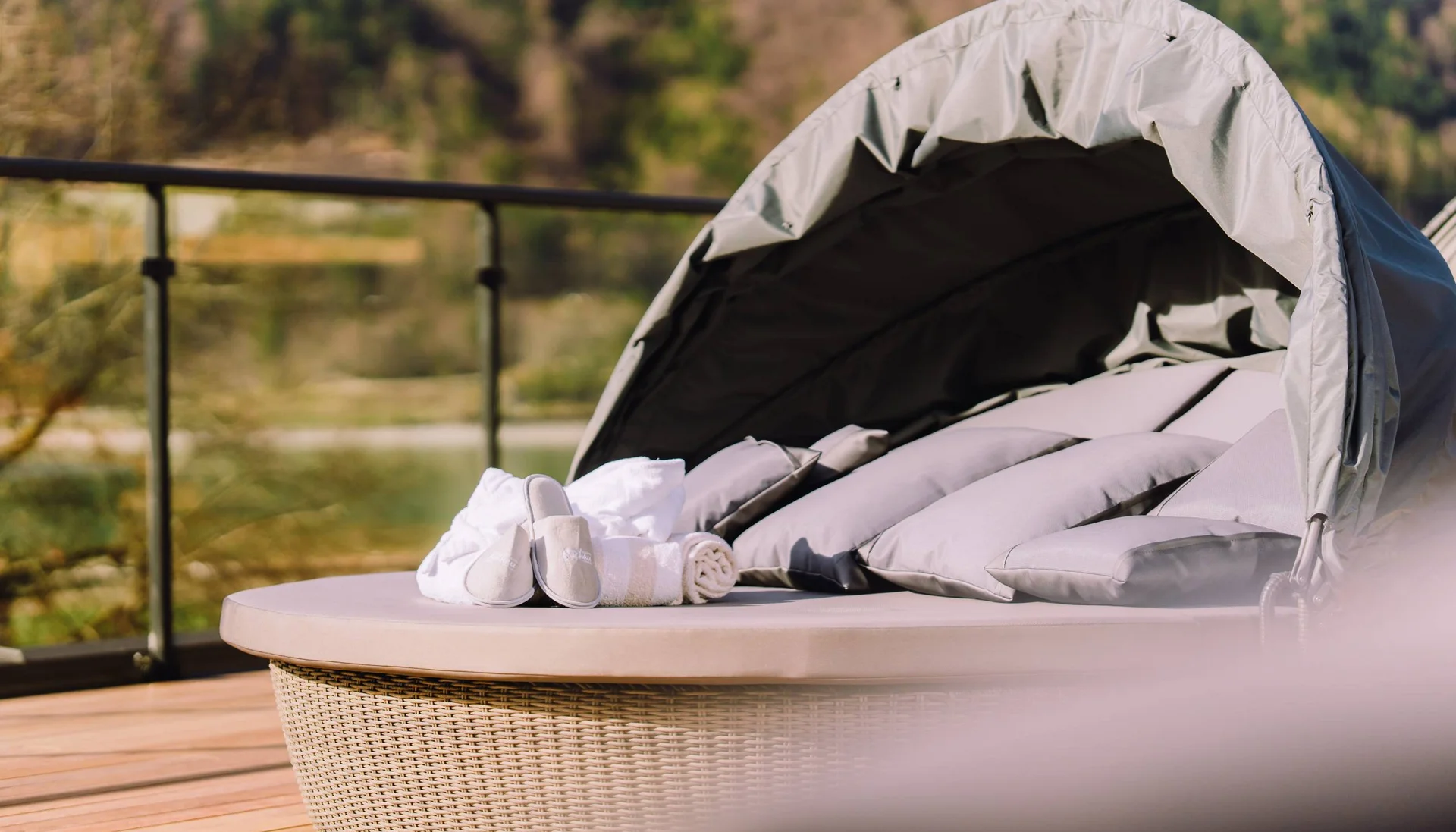 Rundes Loungesofa mit Kissen, Handtüchern und Hausschuhen auf Holzterrasse