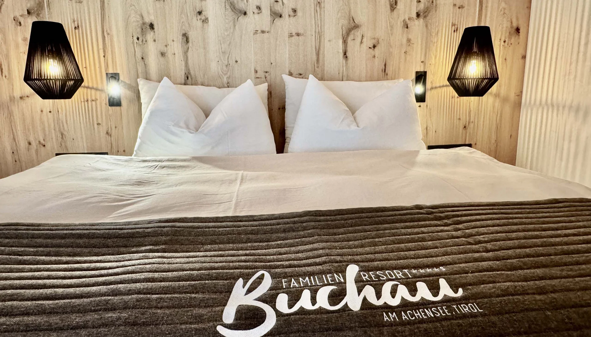Gemütliches Doppelbett mit Holzrückwand und Beleuchtung im Familienresort Buchau Tirol