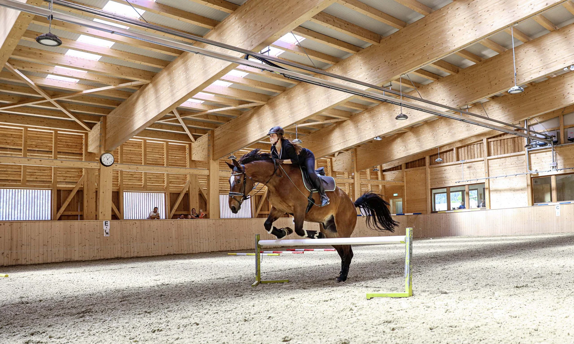 Reiter springt mit Pferd in einer großen Reithalle über Hindernis